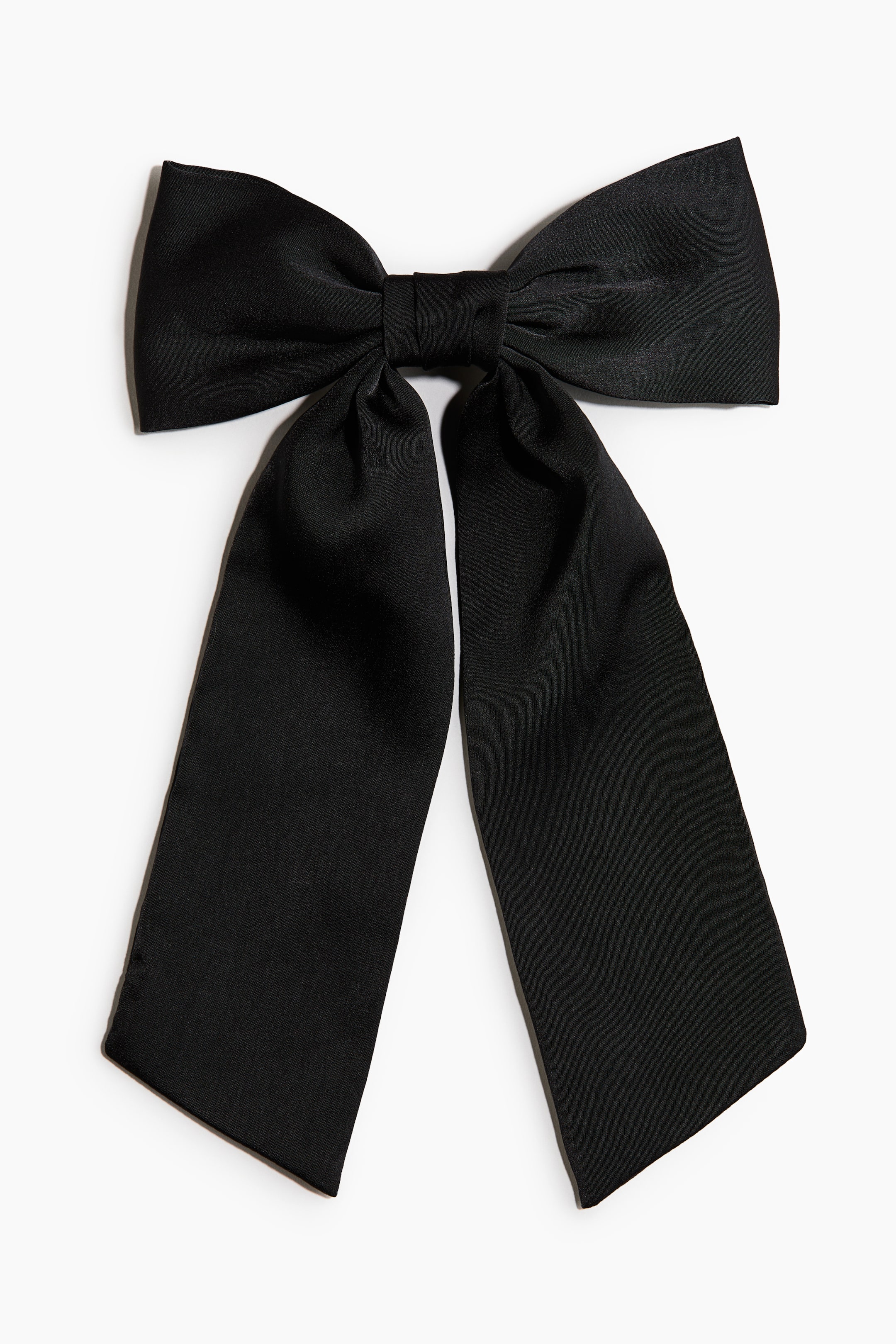 View larger image: A black satin bow faces the front, showing a large structured knot at the centre with two wide loops and two long, flared tails draped downwards. The smooth, slightly lustrous fabric creates soft folds and clean angles along the bottom edges.