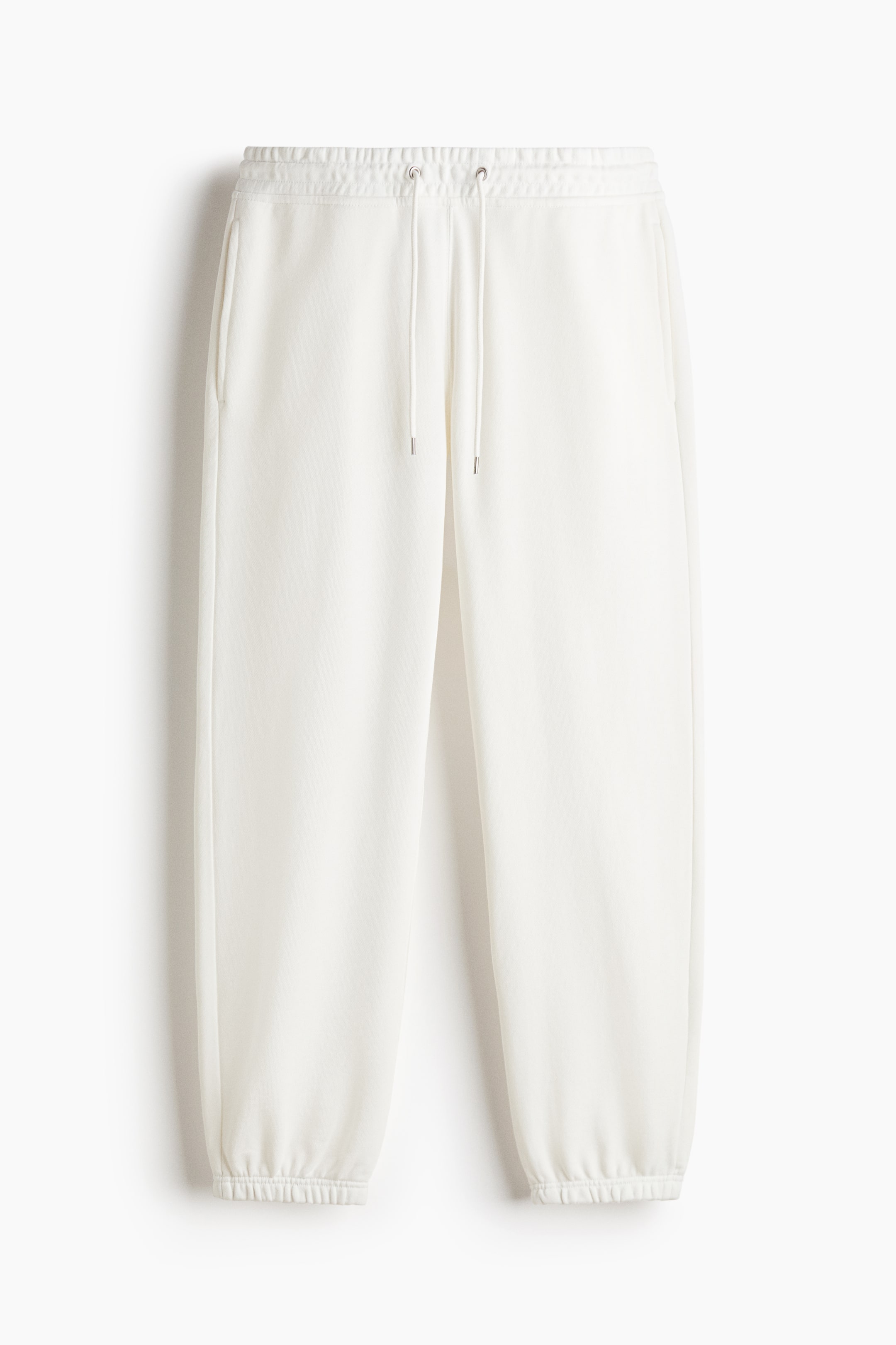 View larger image: Track pants in off-white cotton sweat fabric are shown from the front, featuring a relaxed fit with an elasticated, drawstring waist and elasticated hems. The pants are displaying side-seam pockets and a matching drawstring with silver-toned tips.
