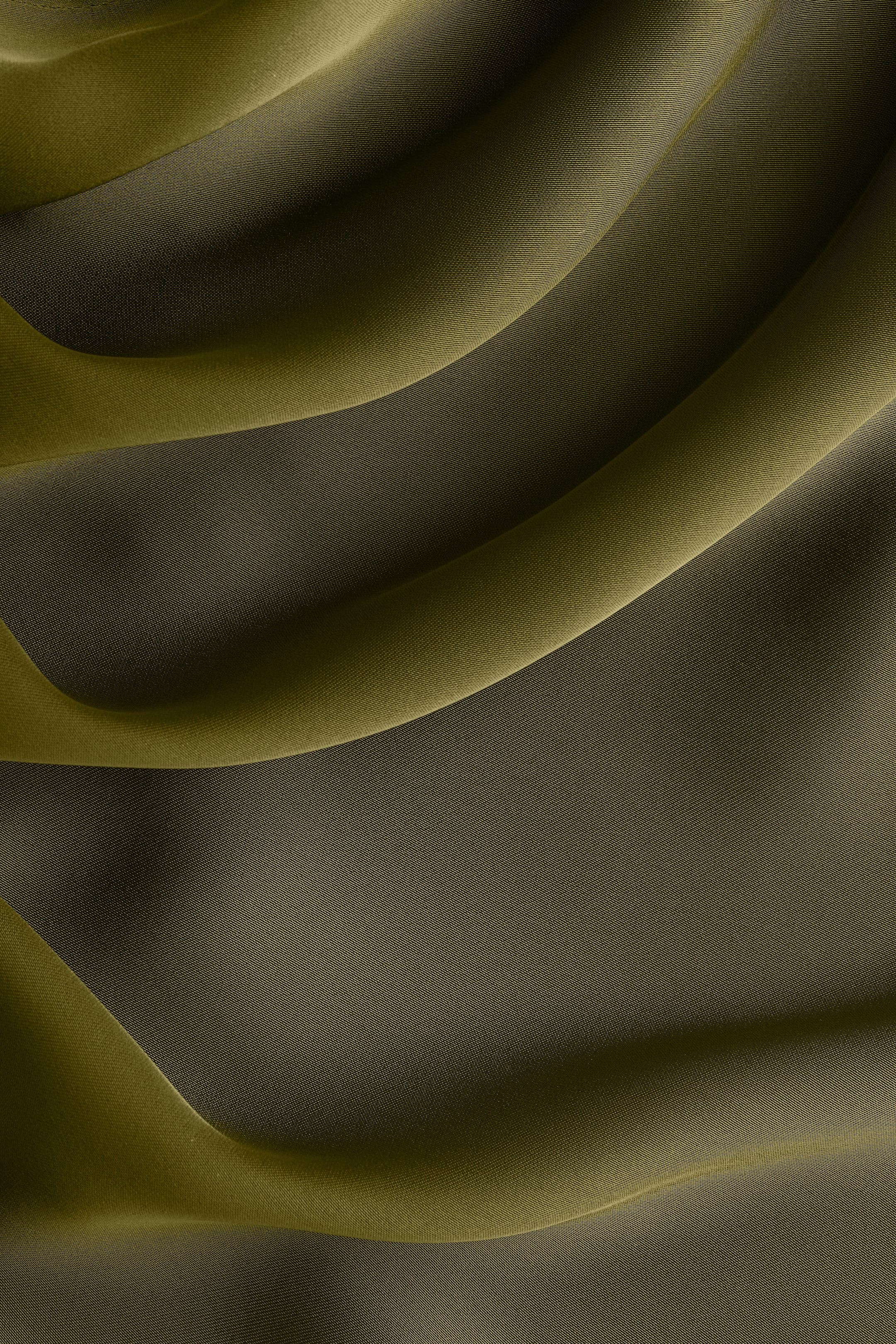 View larger image: The lustrous satin fabric of a blouse is being shown in a close-up, featuring a golden-olive hue with soft, undulating folds creating highlights and shadows.