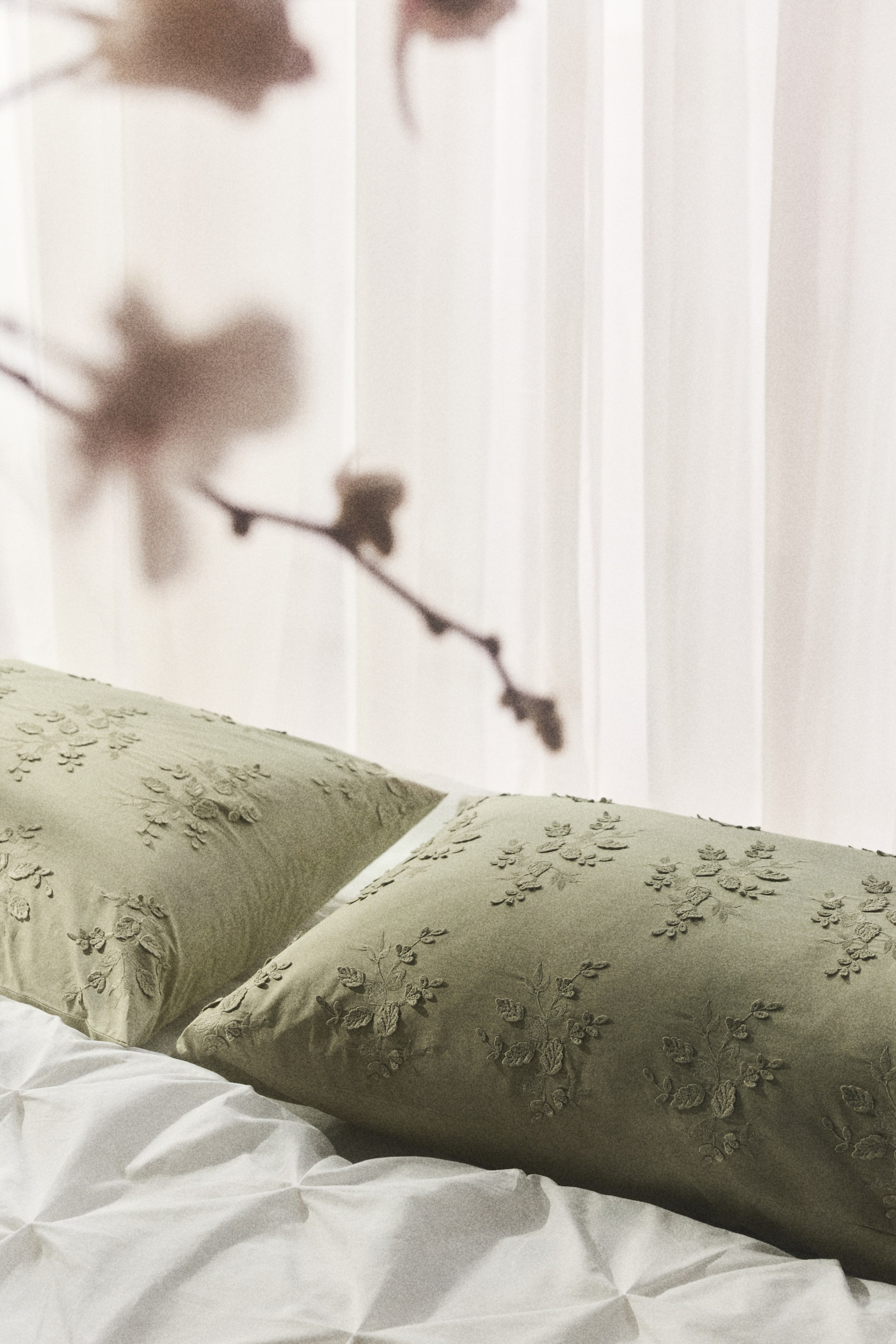 View larger image: Two pillowcases, crafted from a subtle green, textured fabric, showcase elaborate embroidered floral designs across their front surfaces.