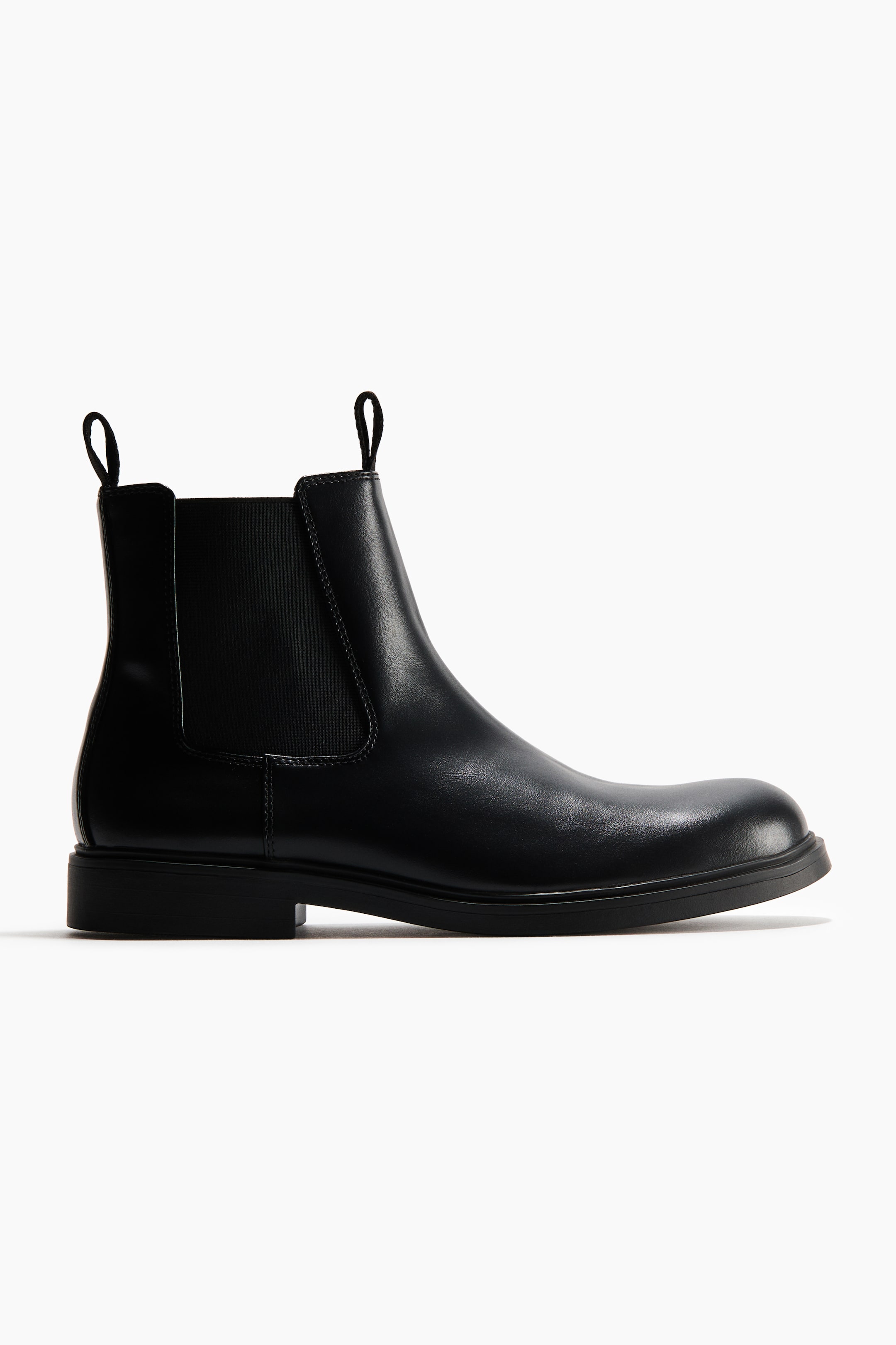 Agrandir l'image: Les bottines Chelsea sont présentées de profil, apparaissant en tissu noir enduit, et sont dotées de goussets latéraux élastiqués, de boucles de tirage à l'avant et à l'arrière, ainsi que de semelles épaisses.