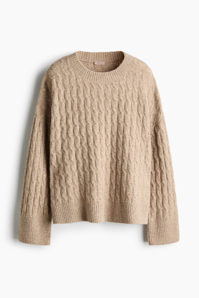 Ein beigefarbener Zopfpullover wird von vorne gezeigt und prÃ¤sentiert eine durchgehend strukturierte Zopfmuster-Optik mit lockerer Passform und Ã¼berschnittenen Schultern. Der Pullover verfÃ¼gt Ã¼ber einen gerippten Rundhalsausschnitt, lange Ãrmel mit breiten gerippten BÃ¼ndchen und einen passenden gerippten Saum. - 1