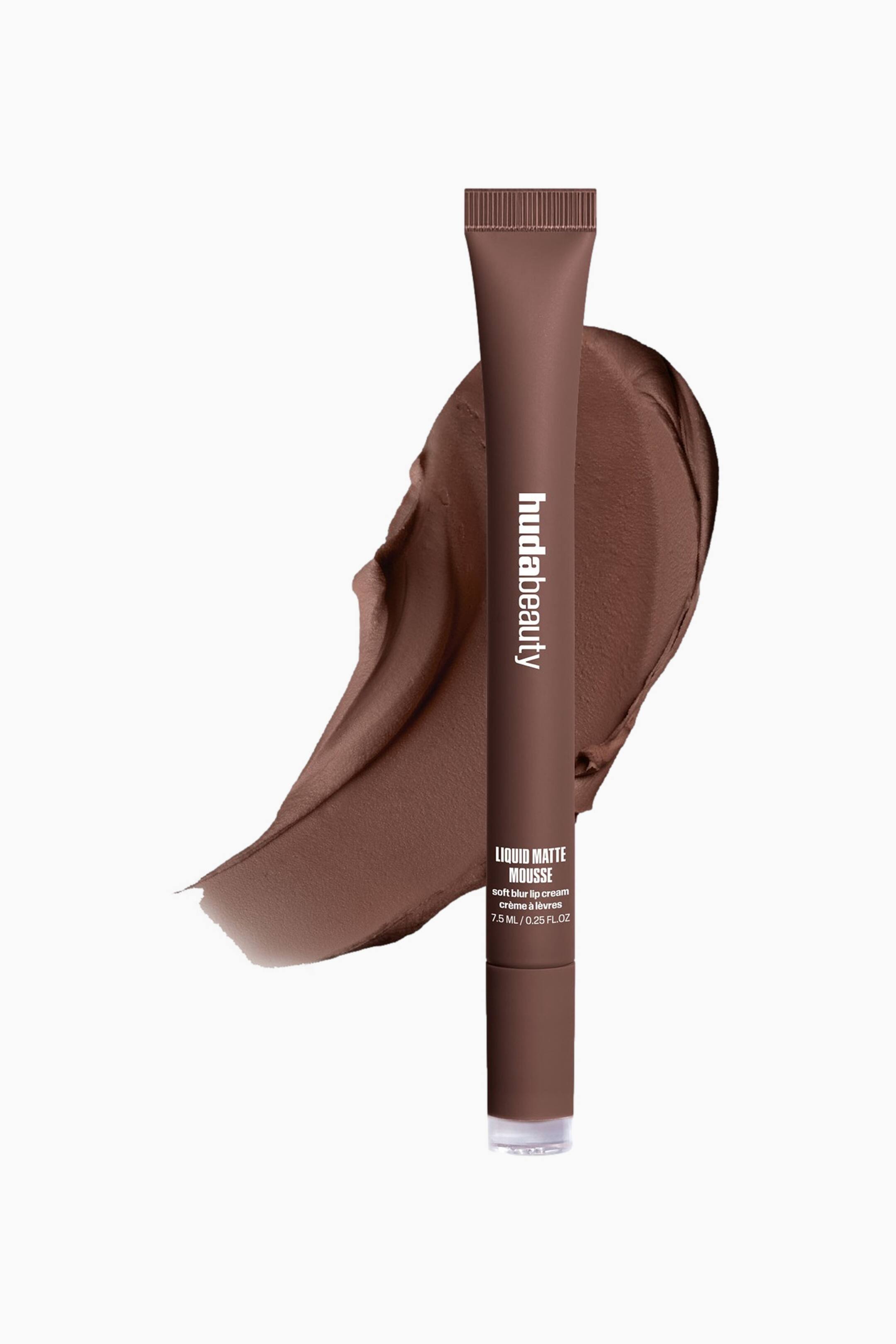 Visa större bild: En chokladbrun tub med Huda Beauty Liquid Matte Mousse står upprätt och lätt vinklad åt höger, med räfflad kork och en genomskinlig bas. Den visar "hudabeauty" vertikalt och "LIQUID MATTE MOUSSE" med produktdetaljer, och vilar mot en virvlad strykning av matchande chokladbrun produkt.