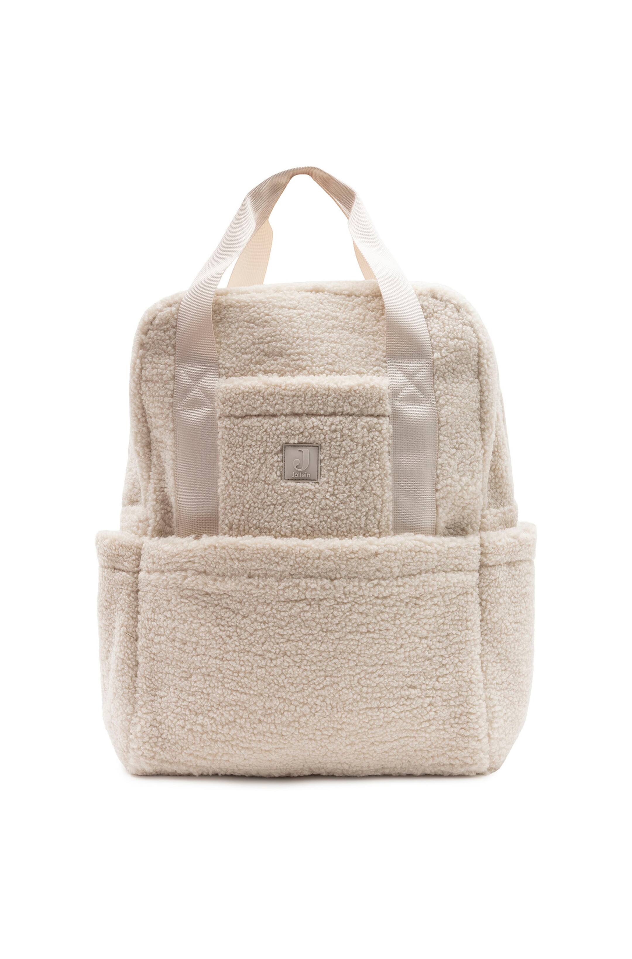 Agrandir l'image: Une vue de face met en valeur un sac à langer à dos en polaire teddy couleur crème, présenté debout. Le sac présente un extérieur sherpa texturé, deux poignées tissées sur le dessus, une petite poche avant supérieure avec un patch logo carré, un grand compartiment avant inférieur et des poches latérales ouvertes.