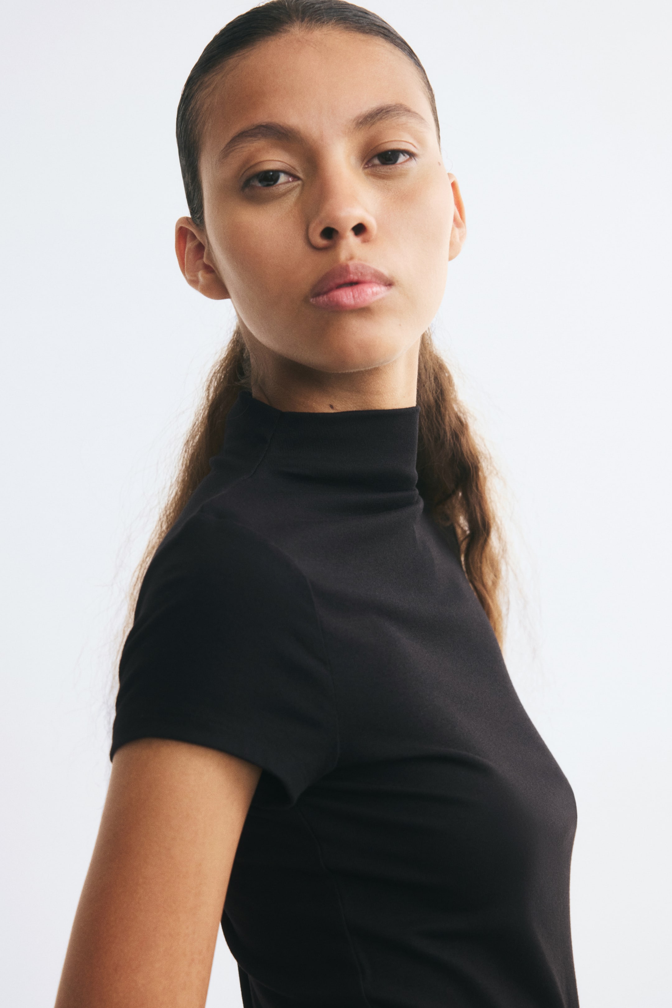 View larger image: The model is wearing a fitted black top featuring a high neck and short cap sleeves.