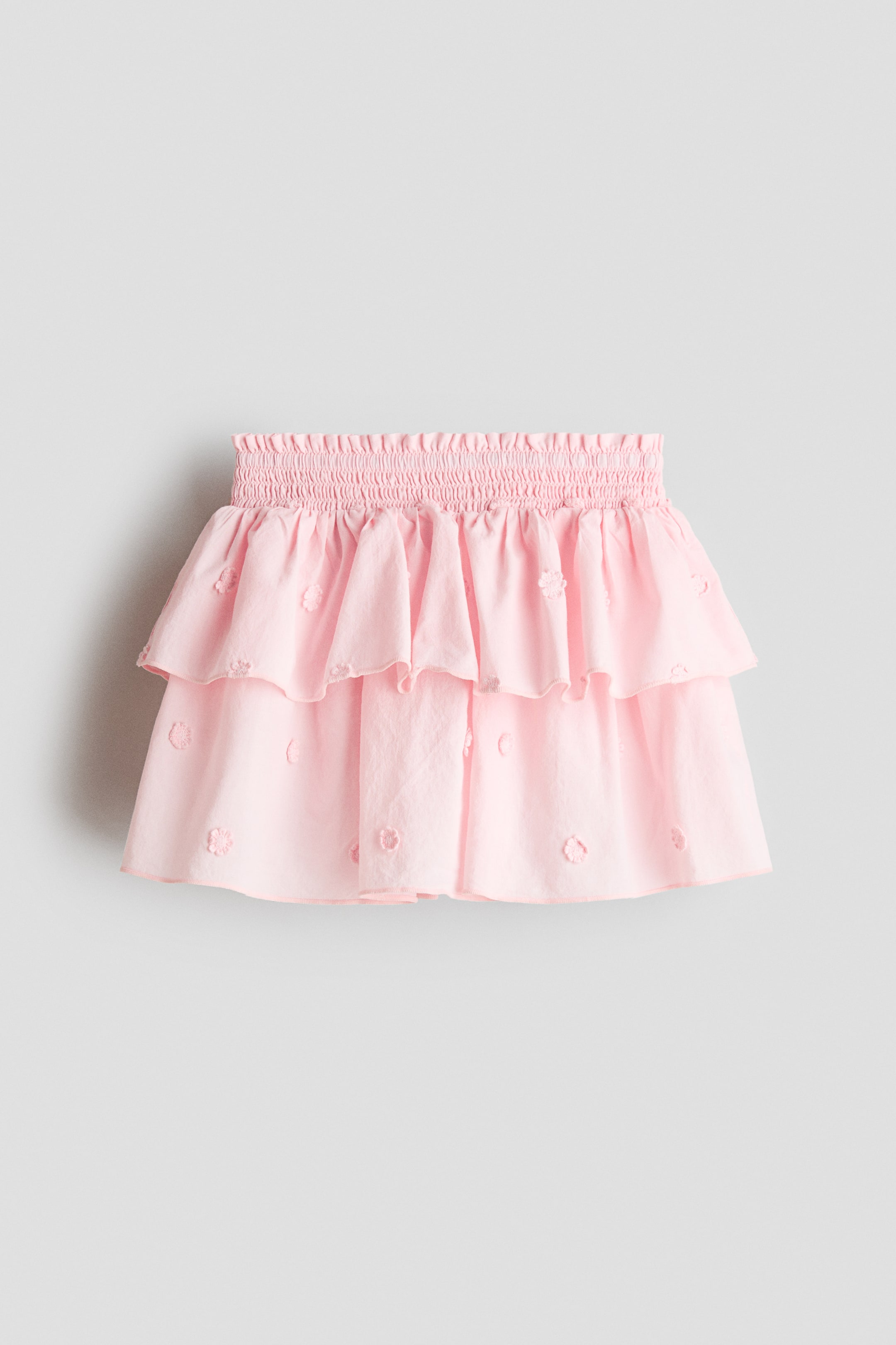 View larger image: Presenting a pink tiered skirt crafted in a breezy weave, showcasing a smocked waistband with a delicate frill trim. It features two ruffled tiers embellished with finely embroidered floral accents.