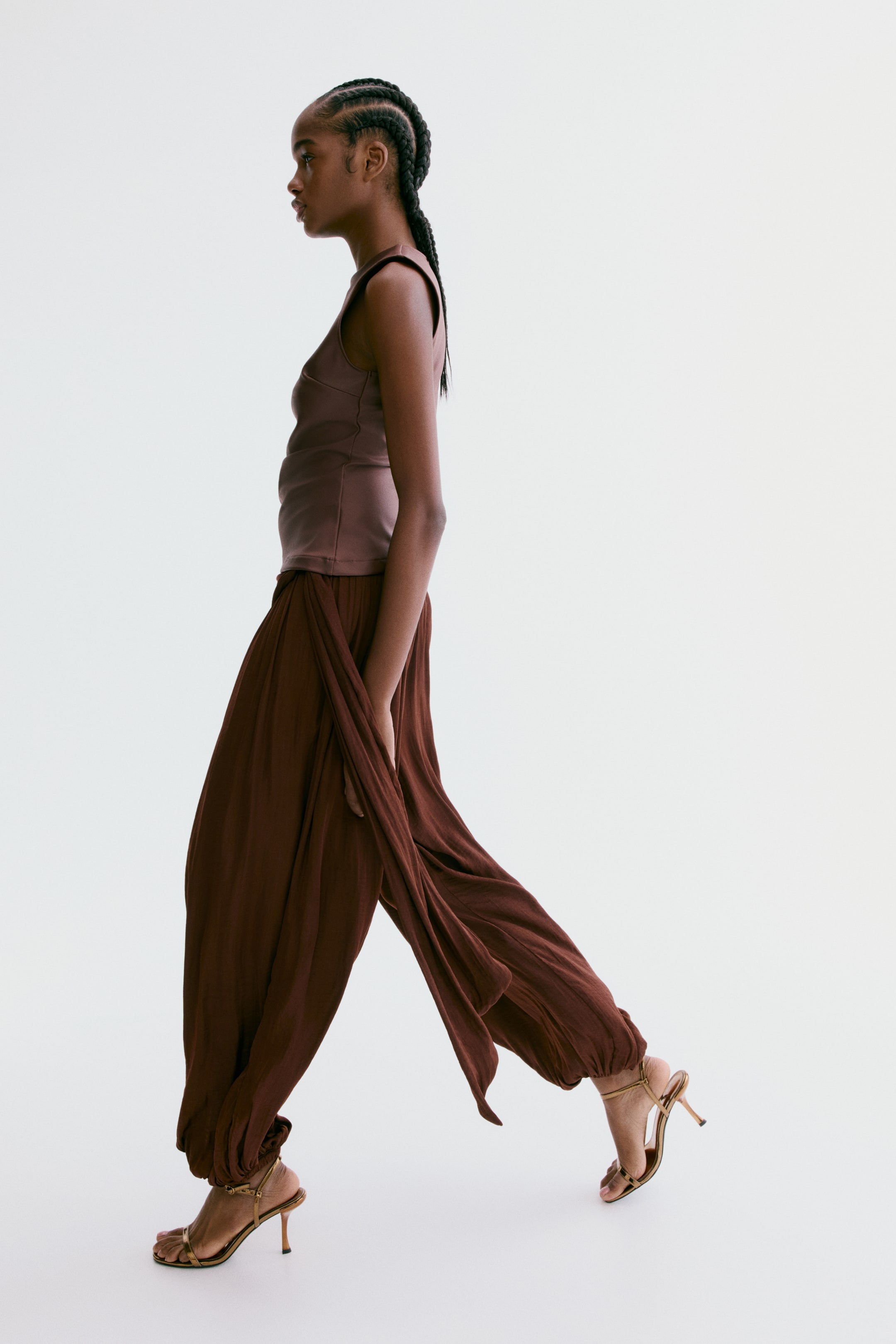 Voir une image plus grande: Le mannequin porte un pantalon ample, longueur cheville, en satin doux et fluide. Il présente une taille élastiquée avec un panneau drapé créant un effet asymétrique et superposé, ainsi que des jambes ballon avec élastication recouverte aux ourlets.