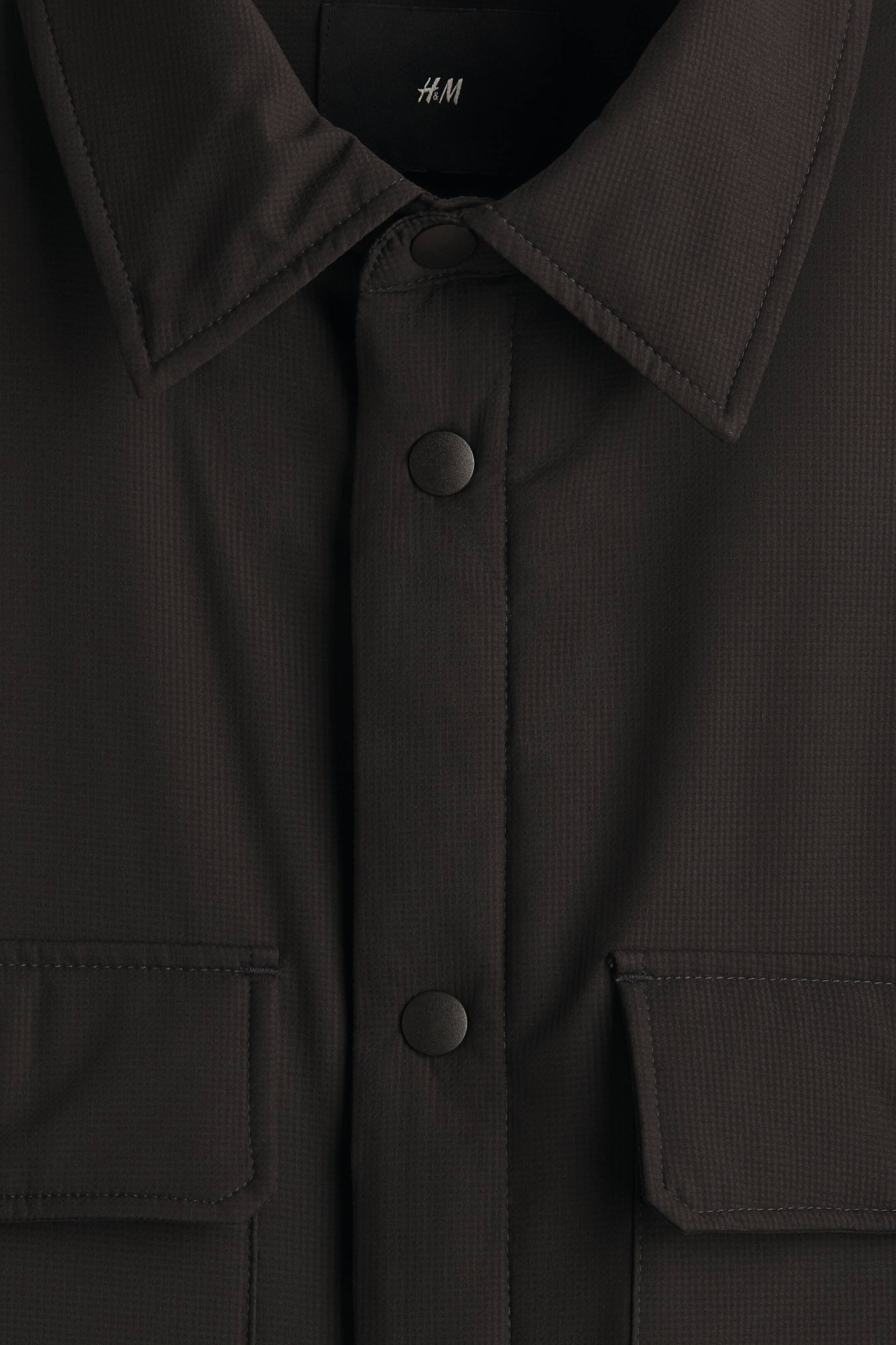 이미지 확대 보기: 어두운 회색 재킷은 앞을 향하고 있으며, 안쪽 칼라에 H&M 라벨이 있는 클래식한 포인트 칼라, 어두운 둥근 버튼이 있는 중앙 플래킷, 그리고 하단에 있는 두 개의 플랩 포켓이 특징이며, 이는 미세한 격자 무늬가 있는 천으로 만들어졌습니다.