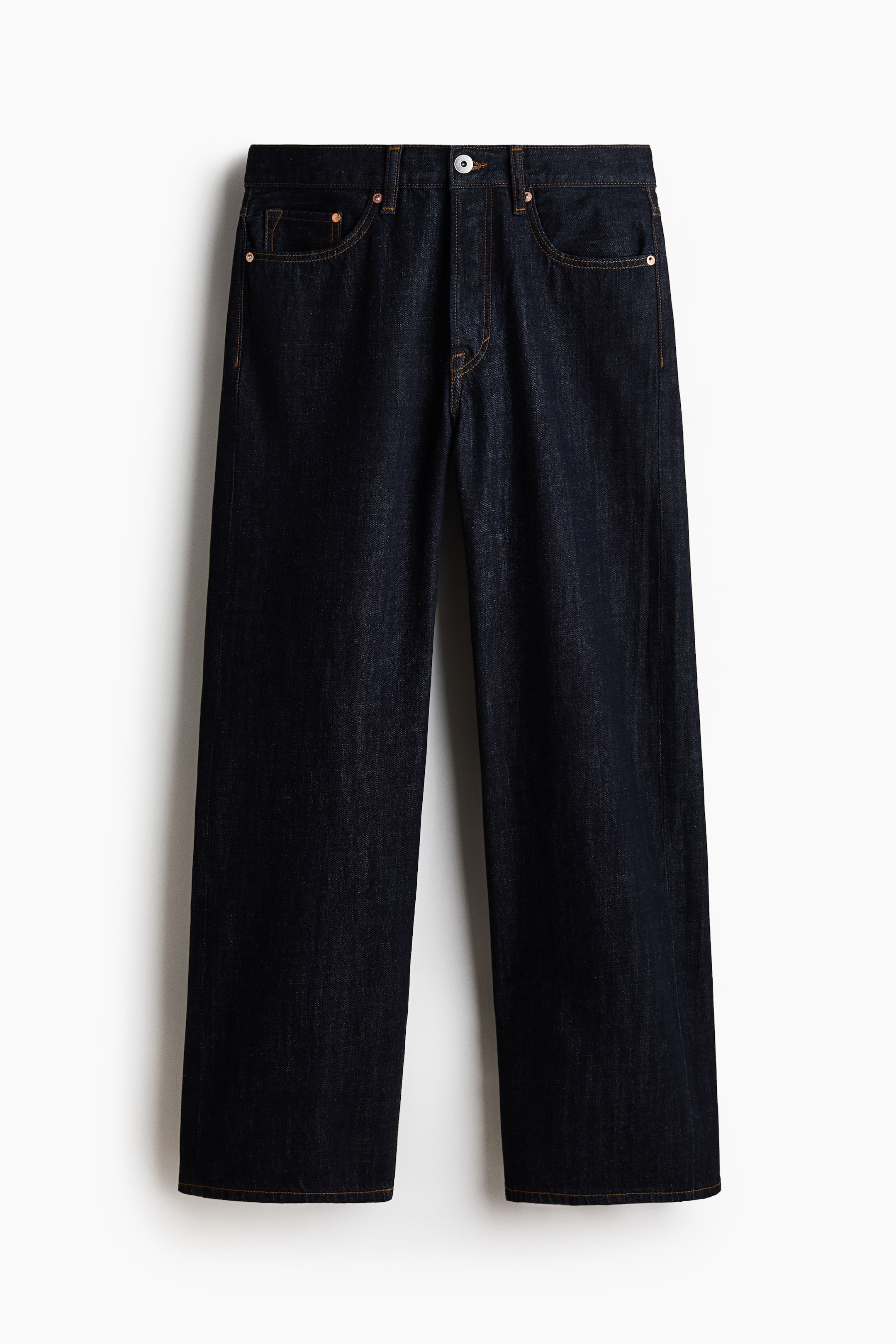 Visa större bild: Mörkblå jeans ligger platt, framåtvända, med en rak benklippning och kontrasterande orange sömmar. De visar upp två framfickor med kopparfärgade nitar, en myntficka och en synlig silverfärgad knappstängning vid midjan.