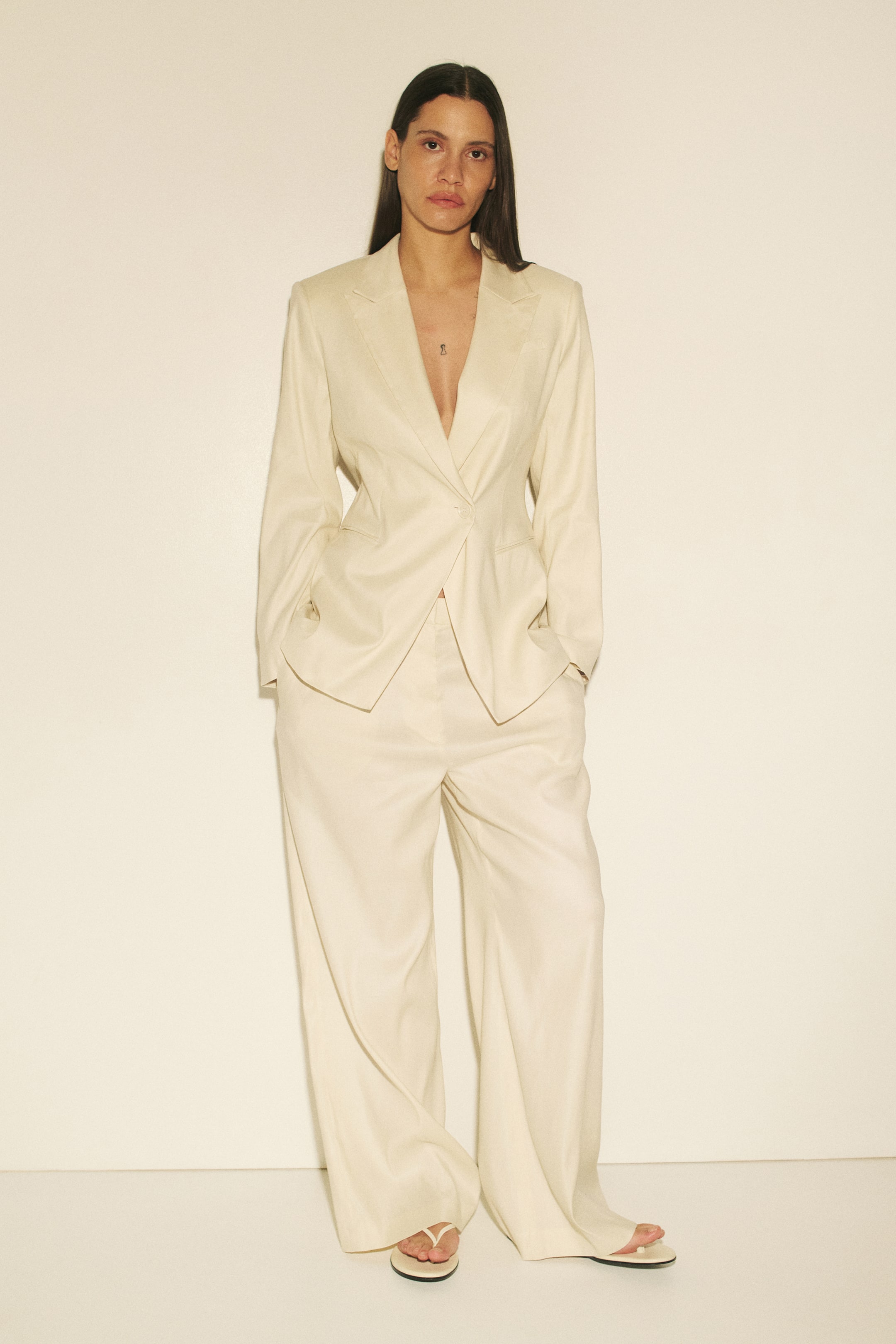 View larger image: "A cream-coloured suit featuring a single-breasted blazer with notch lapels and a single button closure, accompanied by wide-leg trousers. The blazer fits snugly at the waist, while the trousers elegantly flow to the floor."