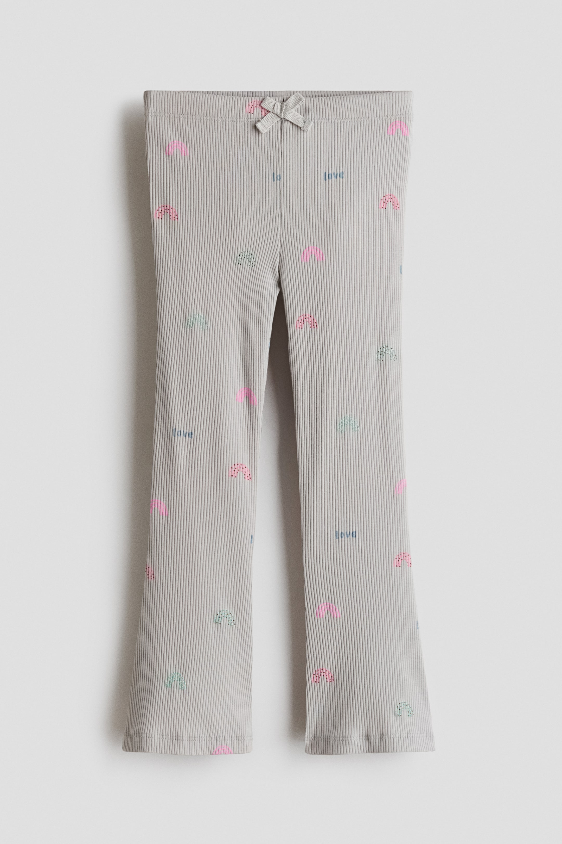 Xem ảnh lớn hơn: Chiếc quần legging cotton jersey gân này được chụp từ phía trước, thể hiện chất vải màu xám nhạt với họa tiết phủ toàn bộ gồm những cầu vồng pastel nhỏ và chữ "love". Thiết kế có cạp chun, được nhấn bằng một chiếc nơ vải nhỏ ở chính giữa phía trước, cùng ống quần hơi loe và gấu quần hoàn thiện bằng đường viền lettuce lượn sóng.