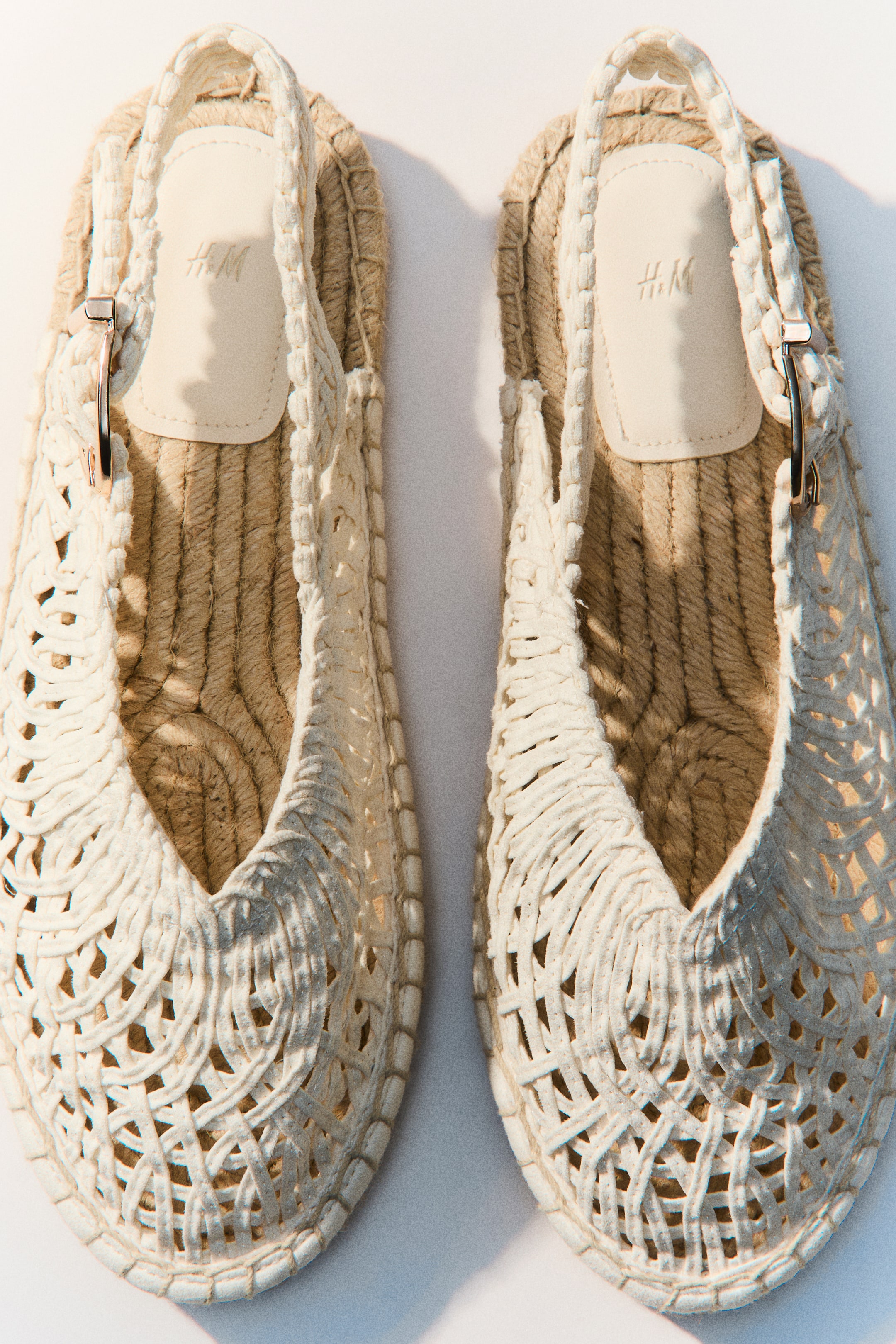 Visa större bild: Ett par espadriller visas från en top-down vinkel, som visar off-white, öppet vävda överdelar och slingback-remmar. Varje rem har ett silvertonat spänne, och skorna visar naturliga jutesulor med en ljusfärgad H&M-logotyp på innersulan.