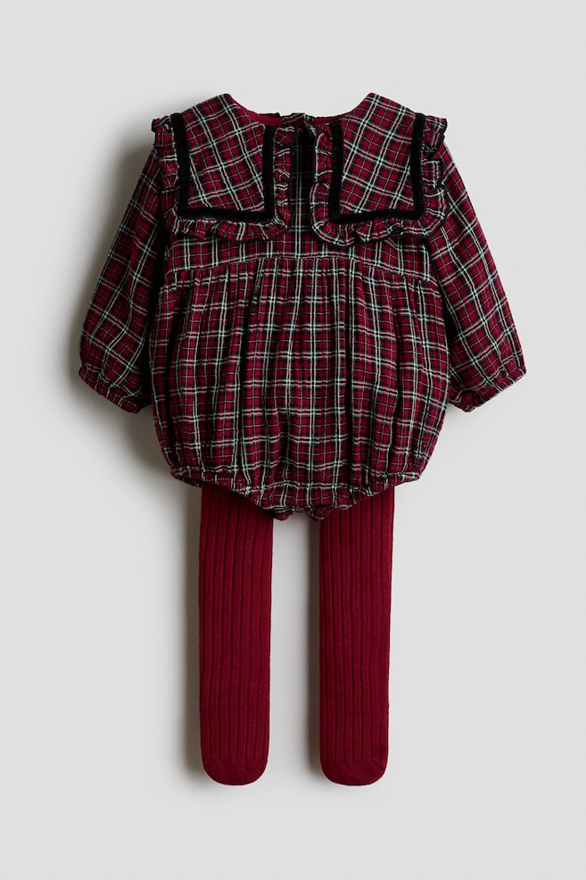 A babyâs outfit featuring a red plaid romper and matching burgundy tights is being displayed from the back. The long-sleeved romper showcases a gathered bubble silhouette and a large ruffled collar with black velvet trim, while the solid-coloured, ribbed tights extend straight down from underneath. - 1
