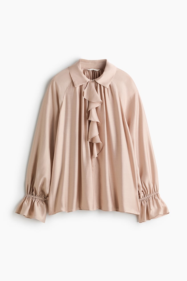 A front-facing, dusty pink blouse is showcasing a pointed collar, a cascading ruffled placket down the center, and a draped, loose-fitting silhouette. It is displaying long, voluminous sleeves gathered with elasticated cuffs that flare into ruffles at the wrists. - 1