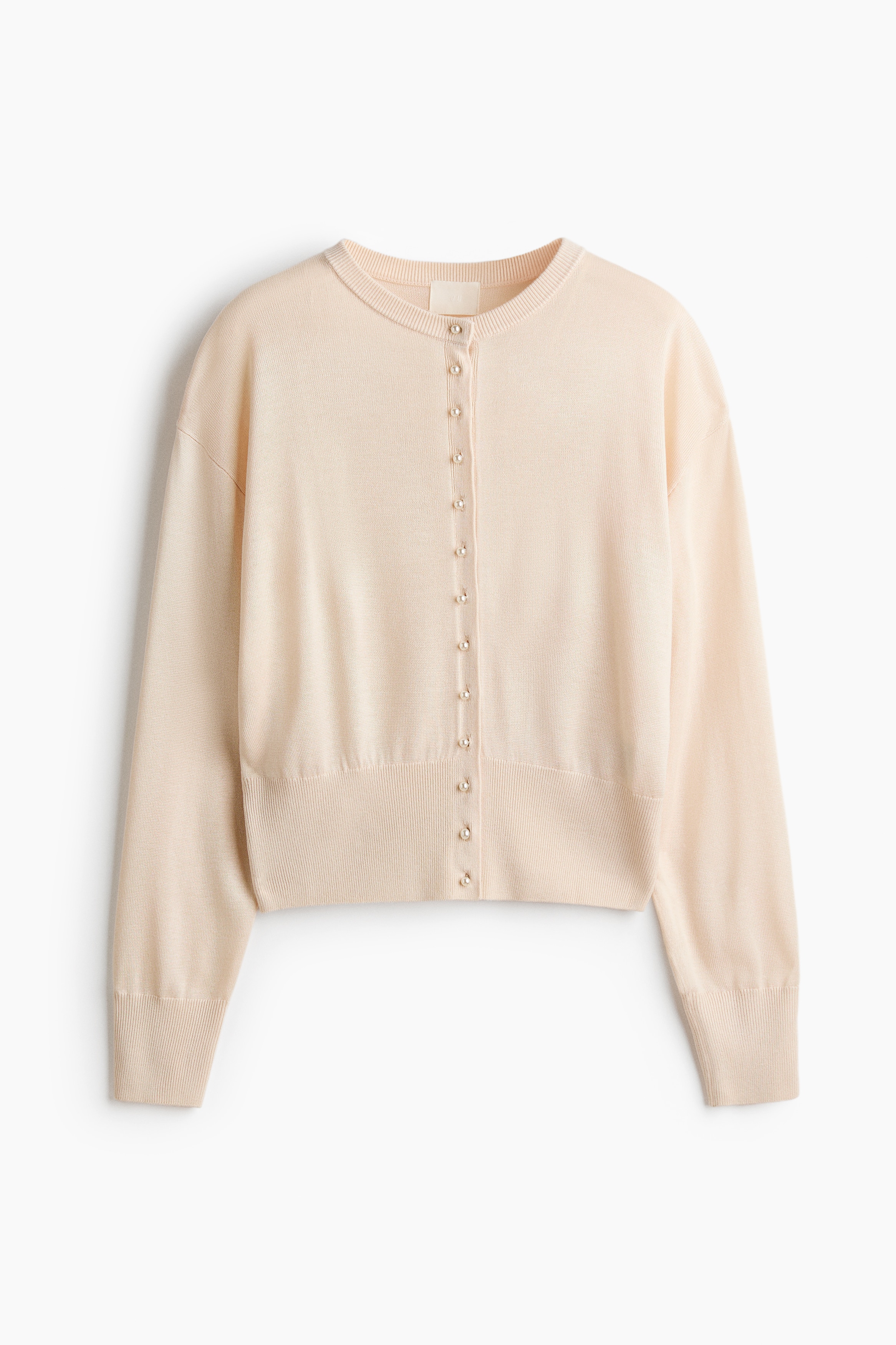 Le mannequin porte un cardigan crÃ¨me clair en maille douce, dotÃ© dâun col rond bordÃ© de cÃ´tes, de boutons nacrÃ©s sur le devant, dâemmanchures tombantes et dâune large ceinture cÃ´telÃ©e. Ce cardigan Ã  manches longues est associÃ© Ã  un jean en denim bleu foncÃ©.