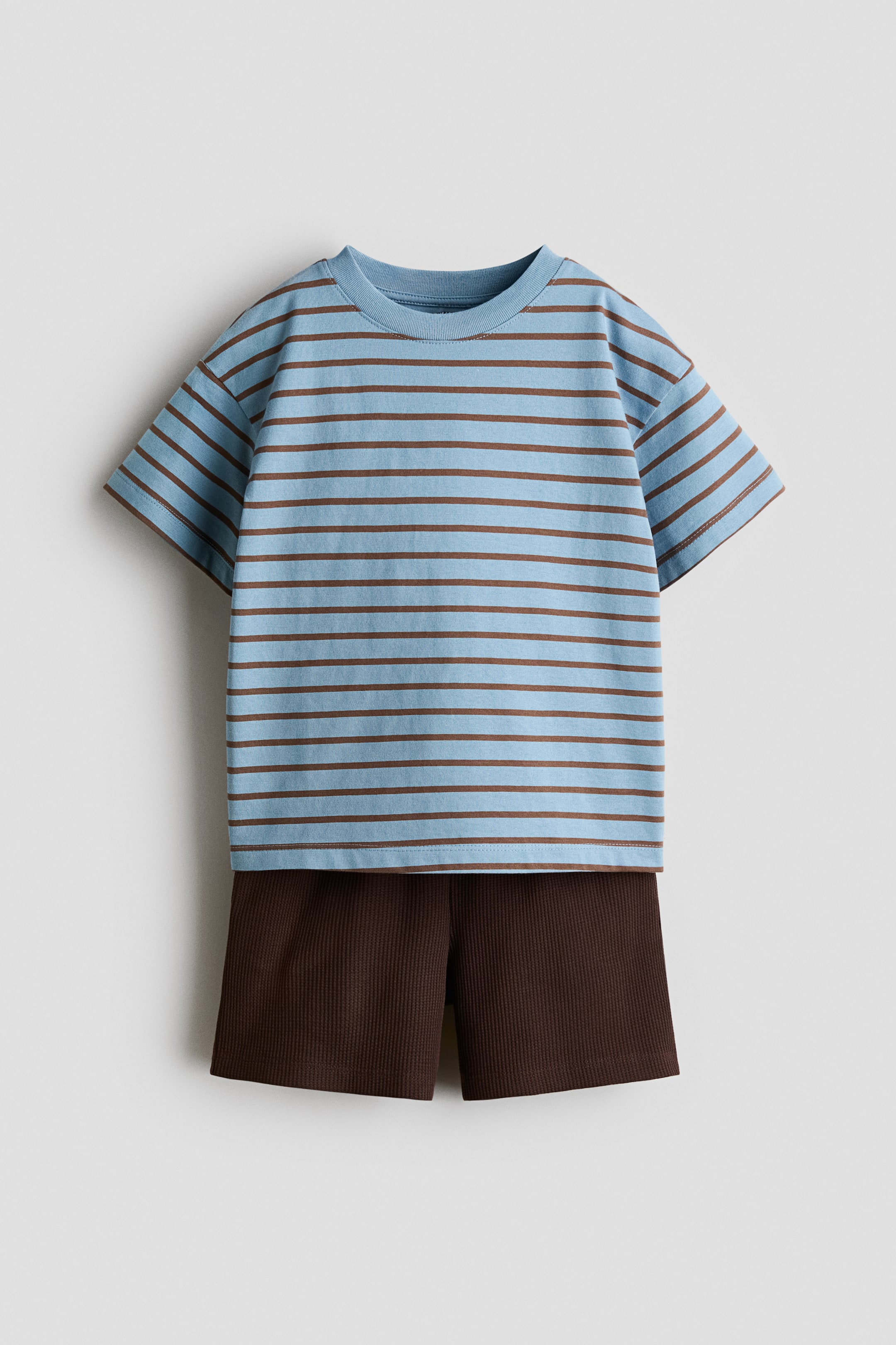 Größeres Bild anzeigen: Dieses zweiteilige Set, von vorne präsentiert, besteht aus einem hellblauen T-Shirt mit kurzen Ärmeln und braunen horizontalen Streifen sowie dunkelbraunen gerippten Shorts. Das gestreifte T-Shirt wird über den strukturierten Shorts getragen.