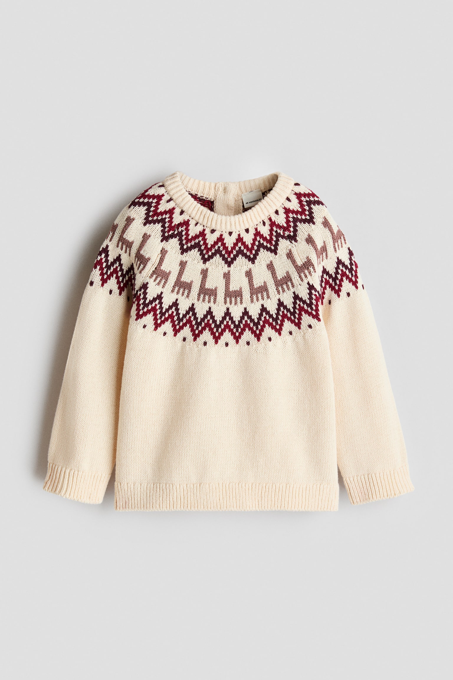Krem renkli Ã¶rme bir kazak Ã¶nden gÃ¶rÃ¼nmektedir; bordo ve kahverengi tonlarÄ±nda, geometrik zikzaklar ve kÃ¼Ã§Ã¼k hayvan motifleri iÃ§eren dekoratif bir Fair Isle omuz detayÄ± sergilemektedir. Kazakta ribana bisiklet yaka, ribana manÅetli uzun kollar ve ribana etek ucu bulunmaktadÄ±r.