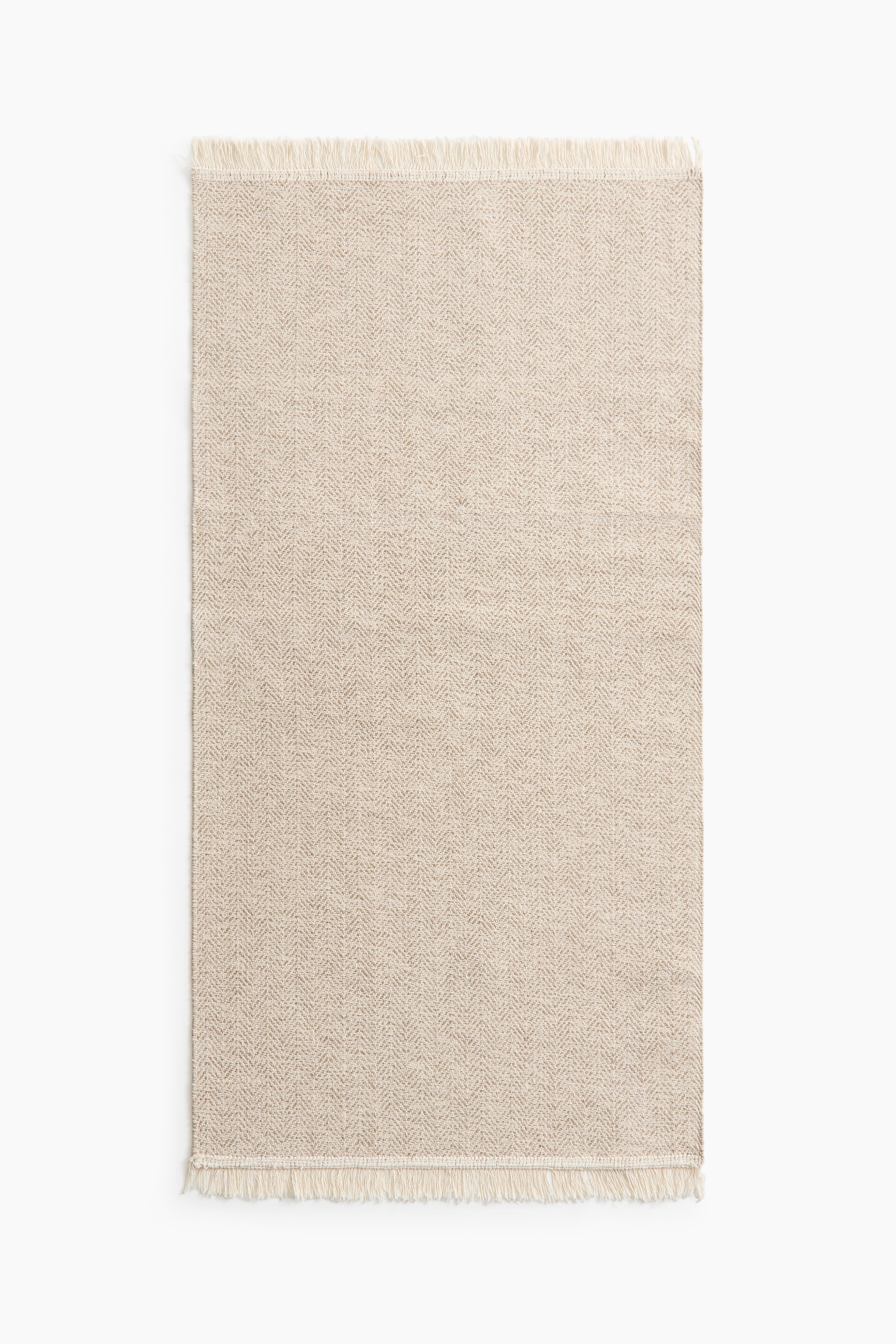 Der Teppich besteht aus einem hellen, gewebten Baumwollmaterial und zeigt ein Fischgrätenmuster. Fransen schmücken seine kurzen Seiten.