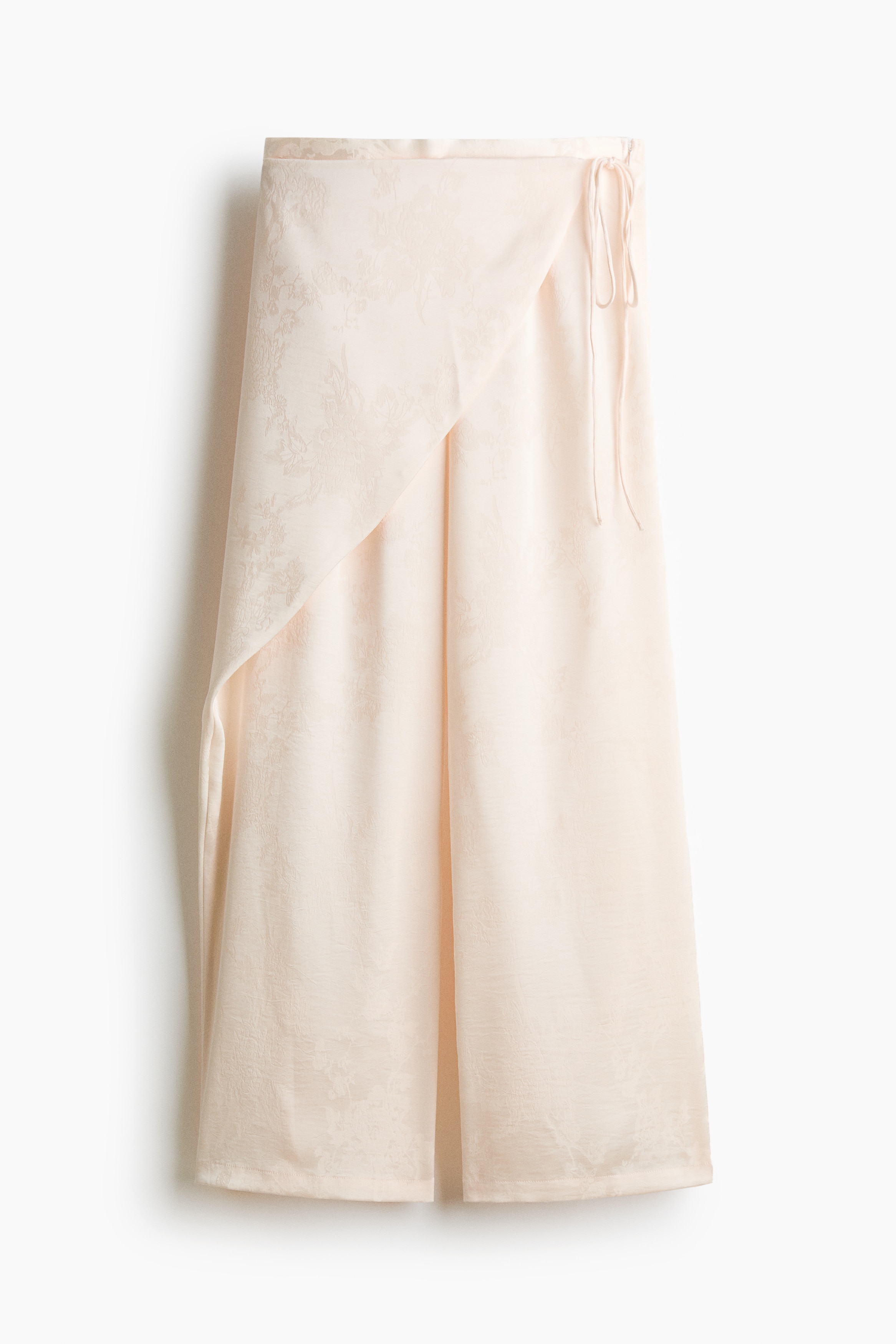 La modelo lleva puestos unos pantalones de tejido jacquard color crema con un detalle de envoltura frontal cosido y delgados lazos tipo spaghetti. Los pantalones de corte recto se combinan con un top a juego de cuello halter con caÃ­da.