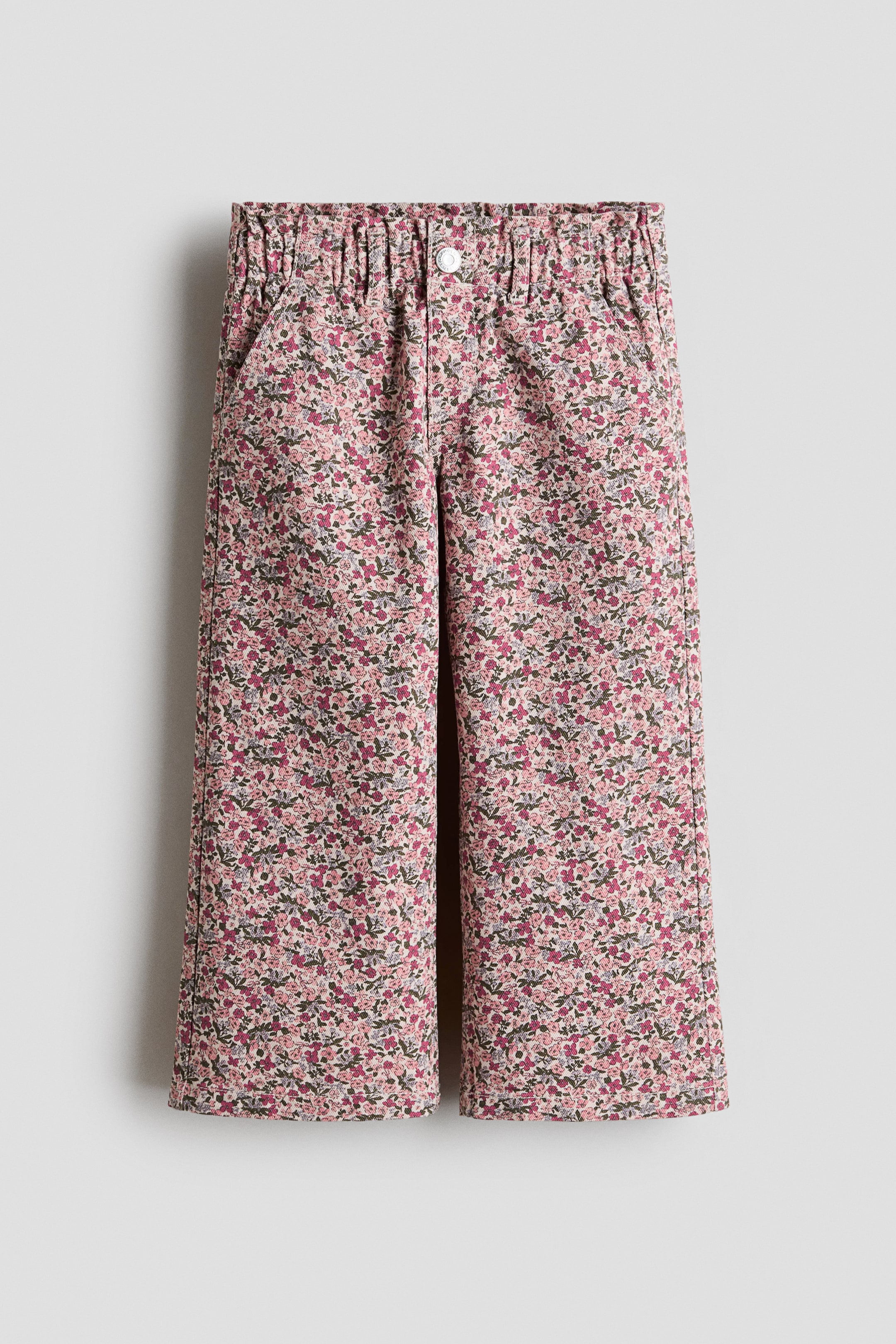 View larger image: These jeans showcase a front view with wide legs and a dense floral pattern in shades of pink, magenta, and green. They are crafted with an elasticated paper bag waist, a faux fly with a white button, and diagonal side pockets.