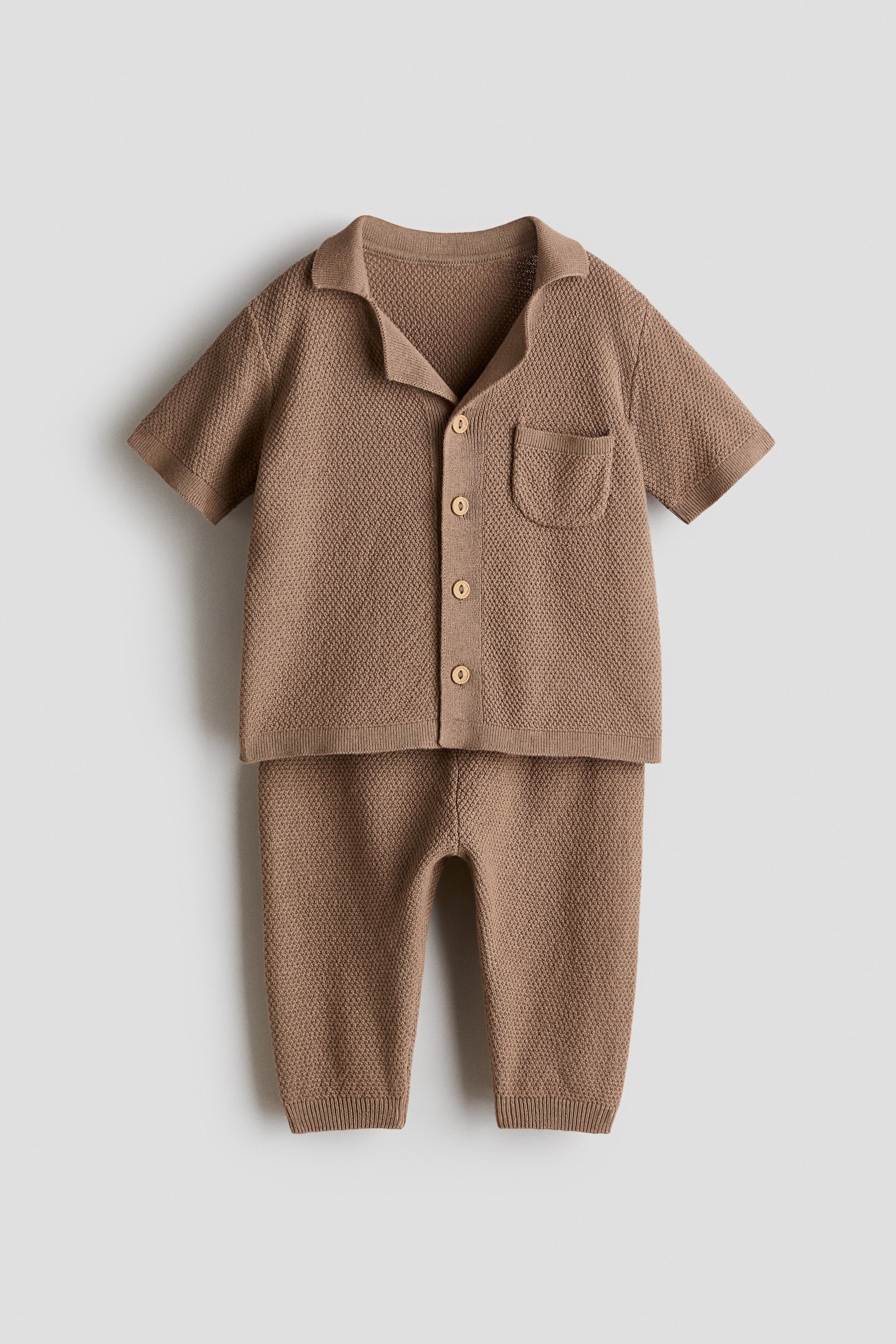 Ver imagen más grande: Se presenta de frente un conjunto de punto de algodón texturizado marrón, compuesto por una camisa de manga corta con cuello tipo resort acanalado, botones delanteros y un bolsillo parche en el pecho, y unos pantalones con bajos acanalados.