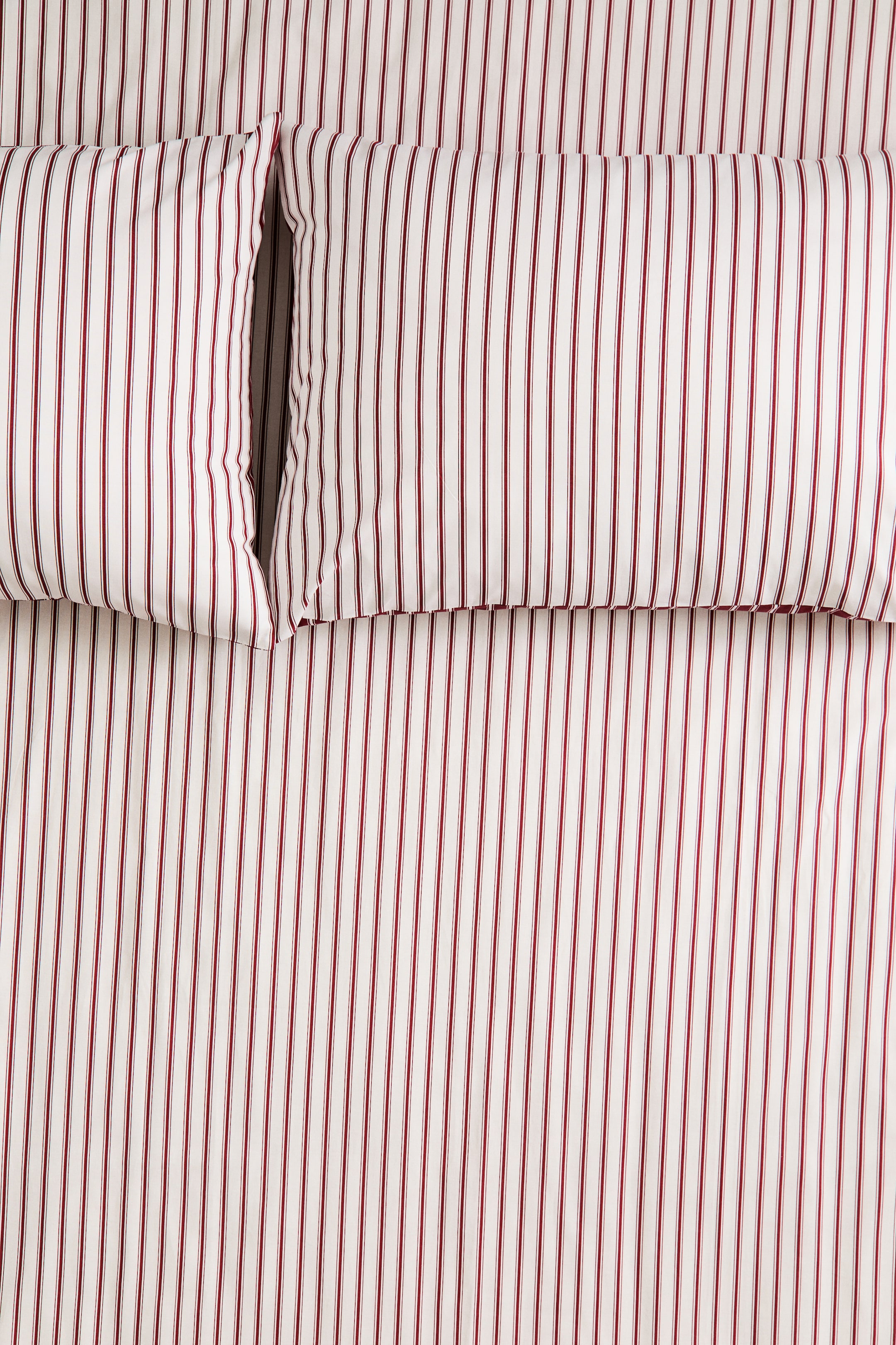 View larger image: A bedding set featuring a white and red vertical ticking stripe pattern is laid flat and viewed from a top-down perspective. Two matching pillows are resting side by side on the coordinating sheet, with the vertical stripes aligned across both the pillows and the sheet.