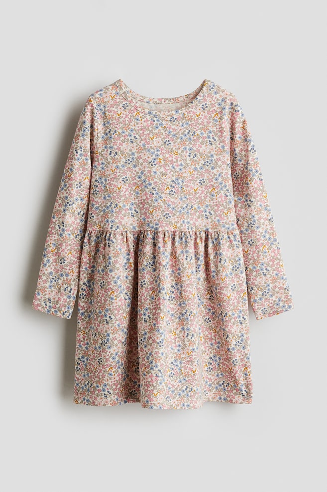 A long-sleeved dress in printed cotton jersey is facing front. It is featuring a floral print in pink, blue, and yellow hues on a light background, a round neckline, a gathered seam at the waist, and a flared skirt. - 1