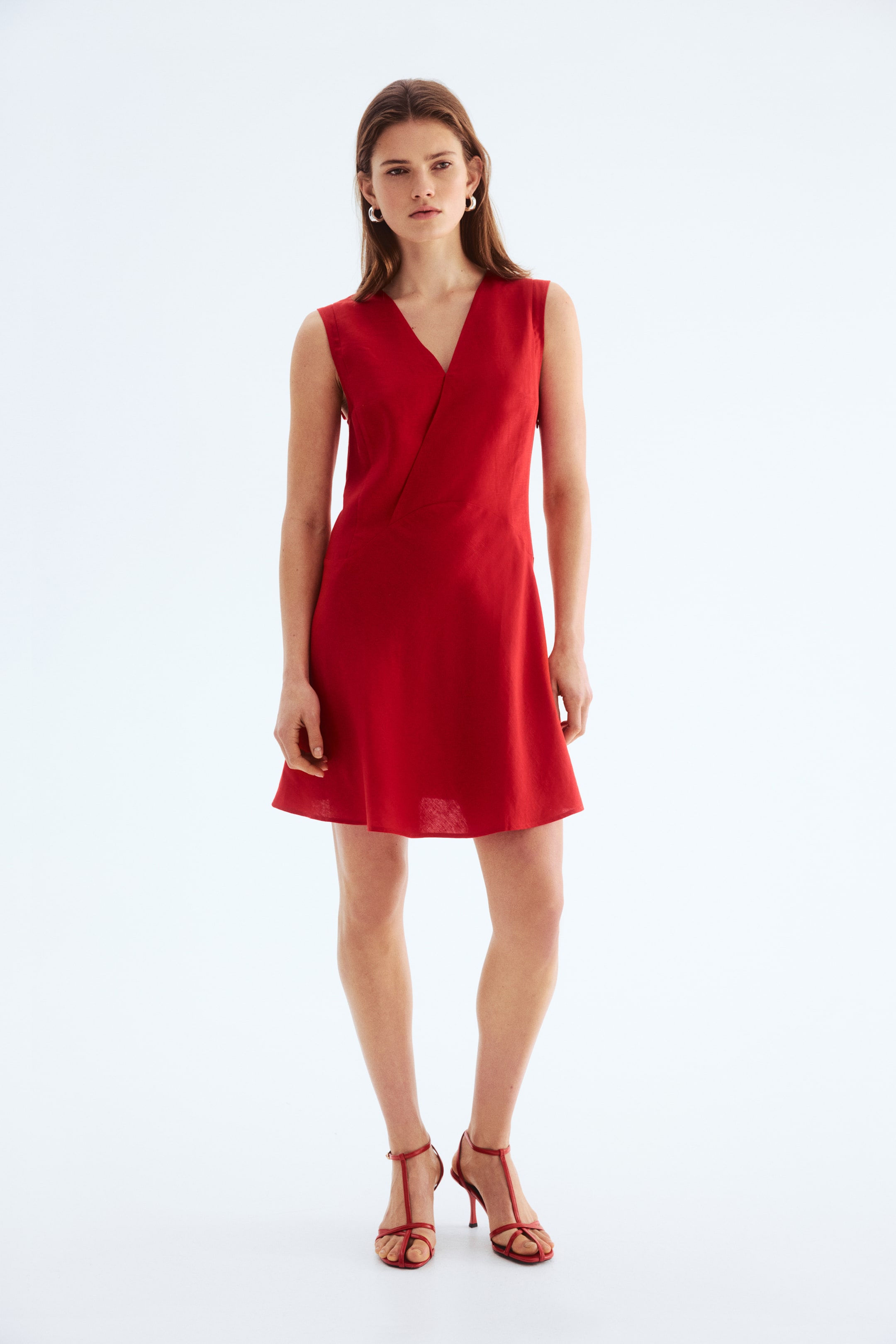 View larger image: A red sleeveless dress features a V-neckline with a faux-wrap bodice, flowing into an A-line mini skirt. The textured dress faces front, showcasing its fitted silhouette.