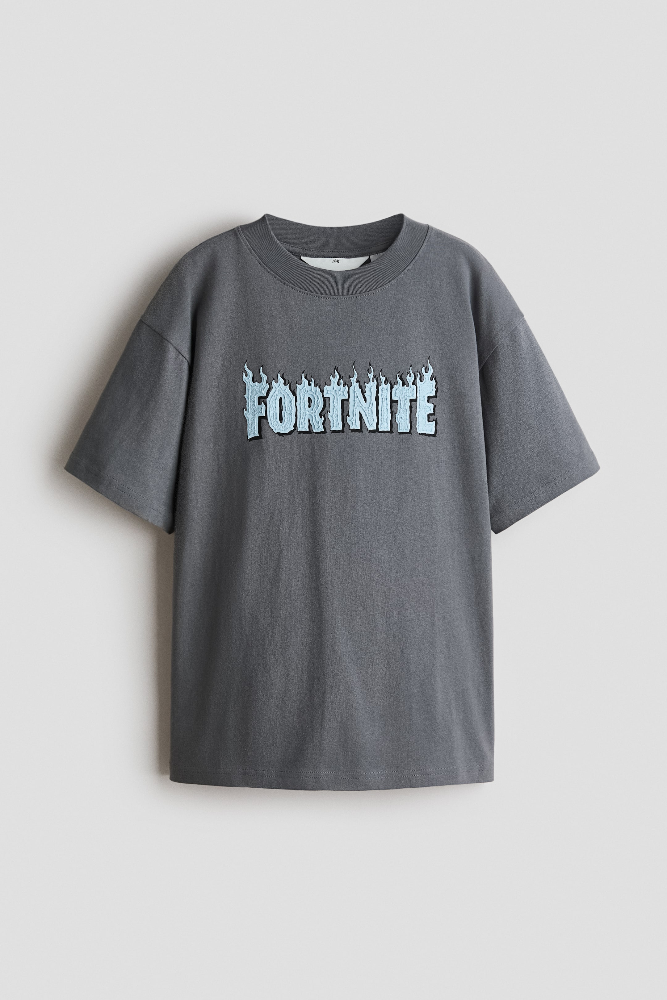 Grotere afbeelding bekijken: Een donkergrijs T-shirt is van voren te zien, met een losse pasvorm, verlaagde schouders en een geribbelde ronde halslijn. Het toont een lichtblauwe 'FORTNITE' grafische print met vlamachtige details aan de voorkant.