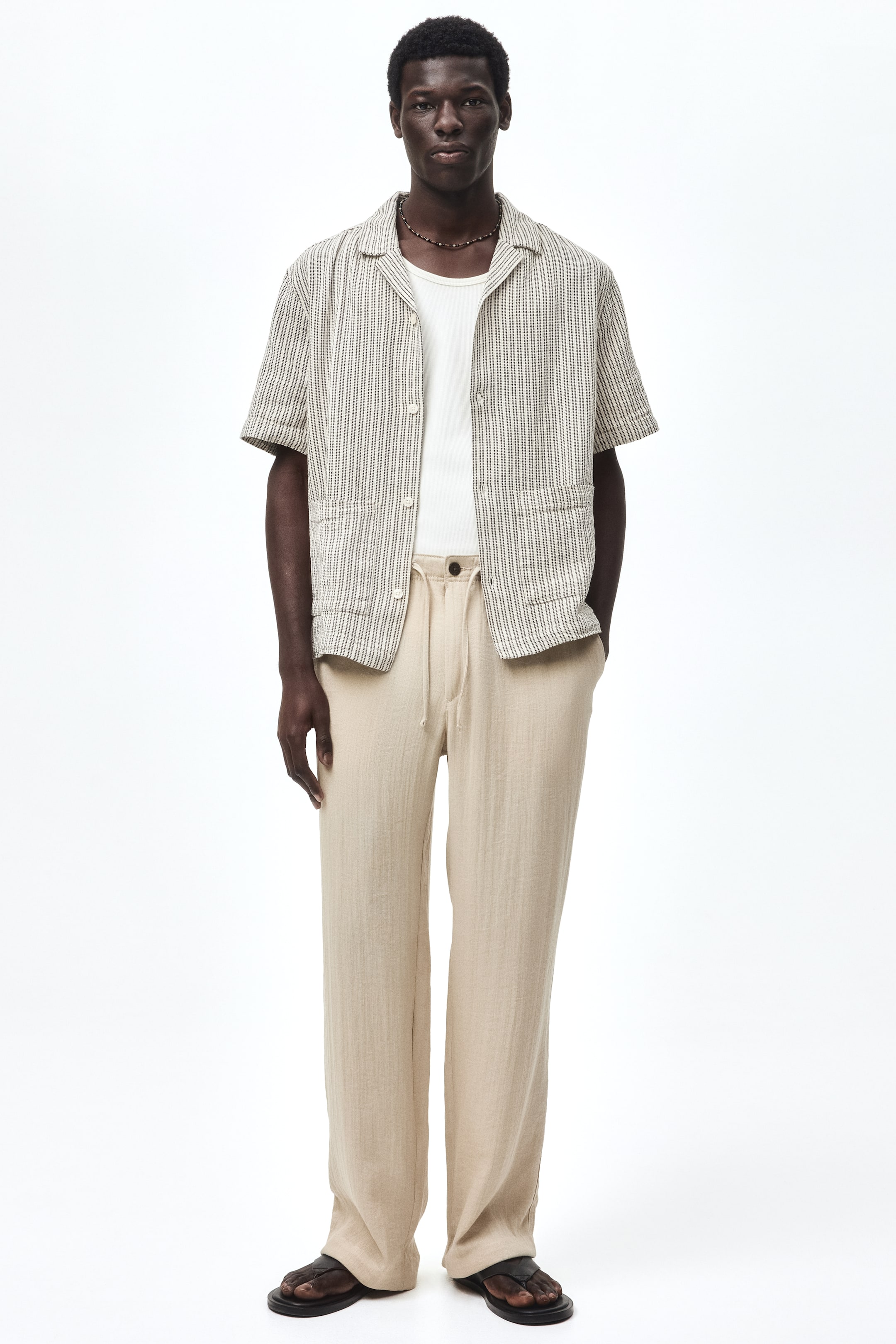 View larger image: A pair of light beige, full-length, wide-leg pants is shown front-facing, featuring a subtle vertical texture and a drawstring waist.