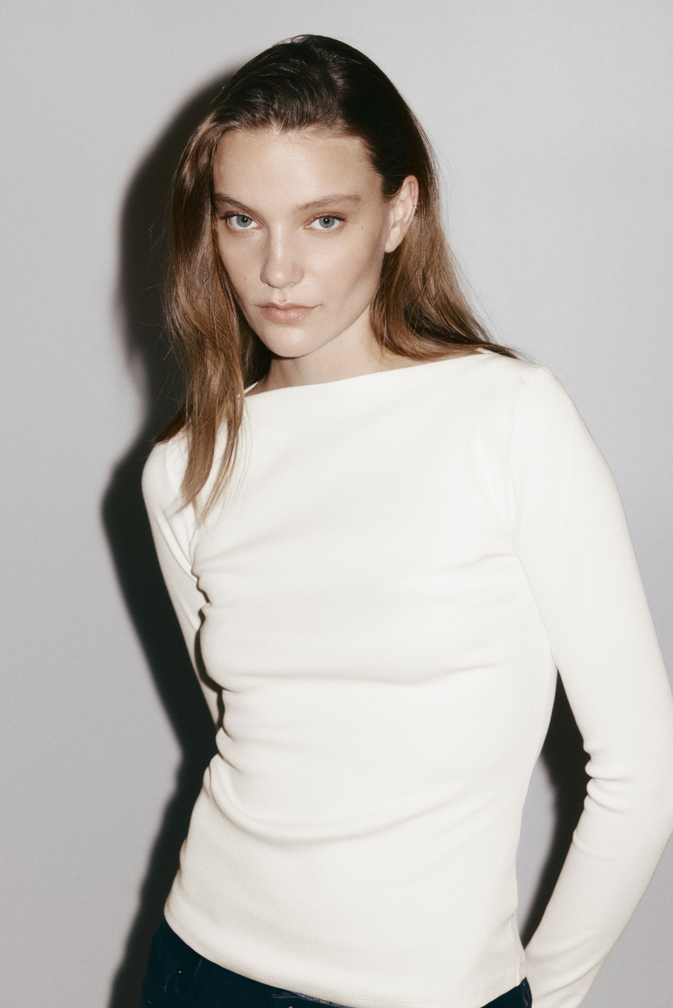 View larger image: A white, ribbed, long-sleeved top is shown from a slight angle, highlighting its boat neckline and figure-hugging silhouette.