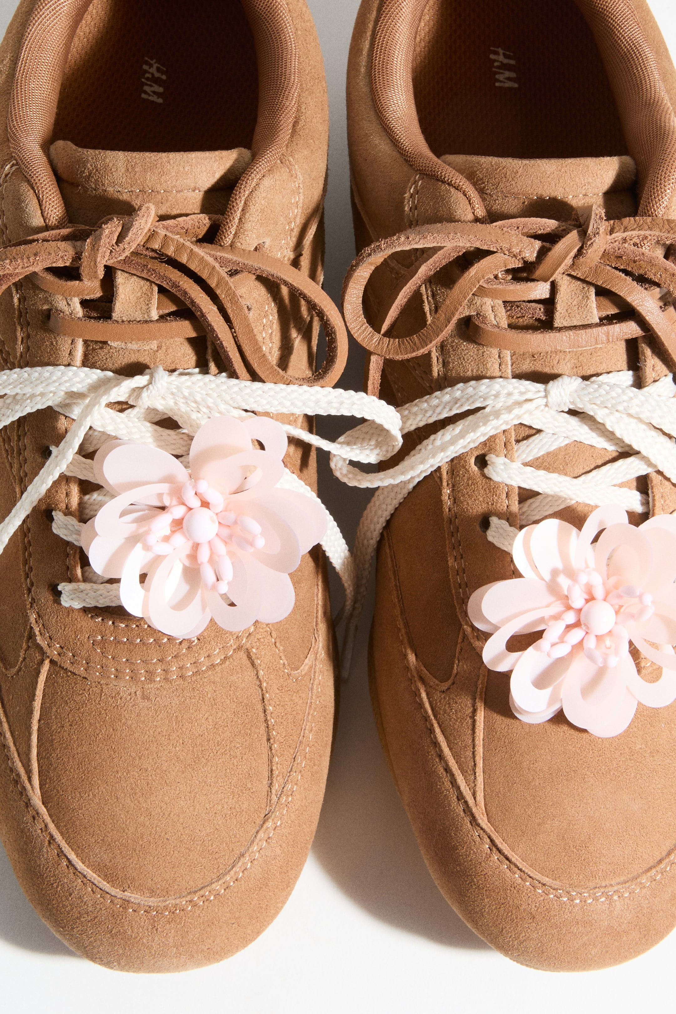 Προβολή μεγαλύτερης εικόνας: Λουλούδια-σχήματος διακοσμητικά για παπούτσια, με ημιδιαφανή ροζ, πολυεπίπεδα πέταλα και υφή στο κέντρο, στερεώνονται με κούμπωμα τύπου "spring ring" σε λευκά κορδόνια πάνω σε καφέ σουέτ παπούτσια.