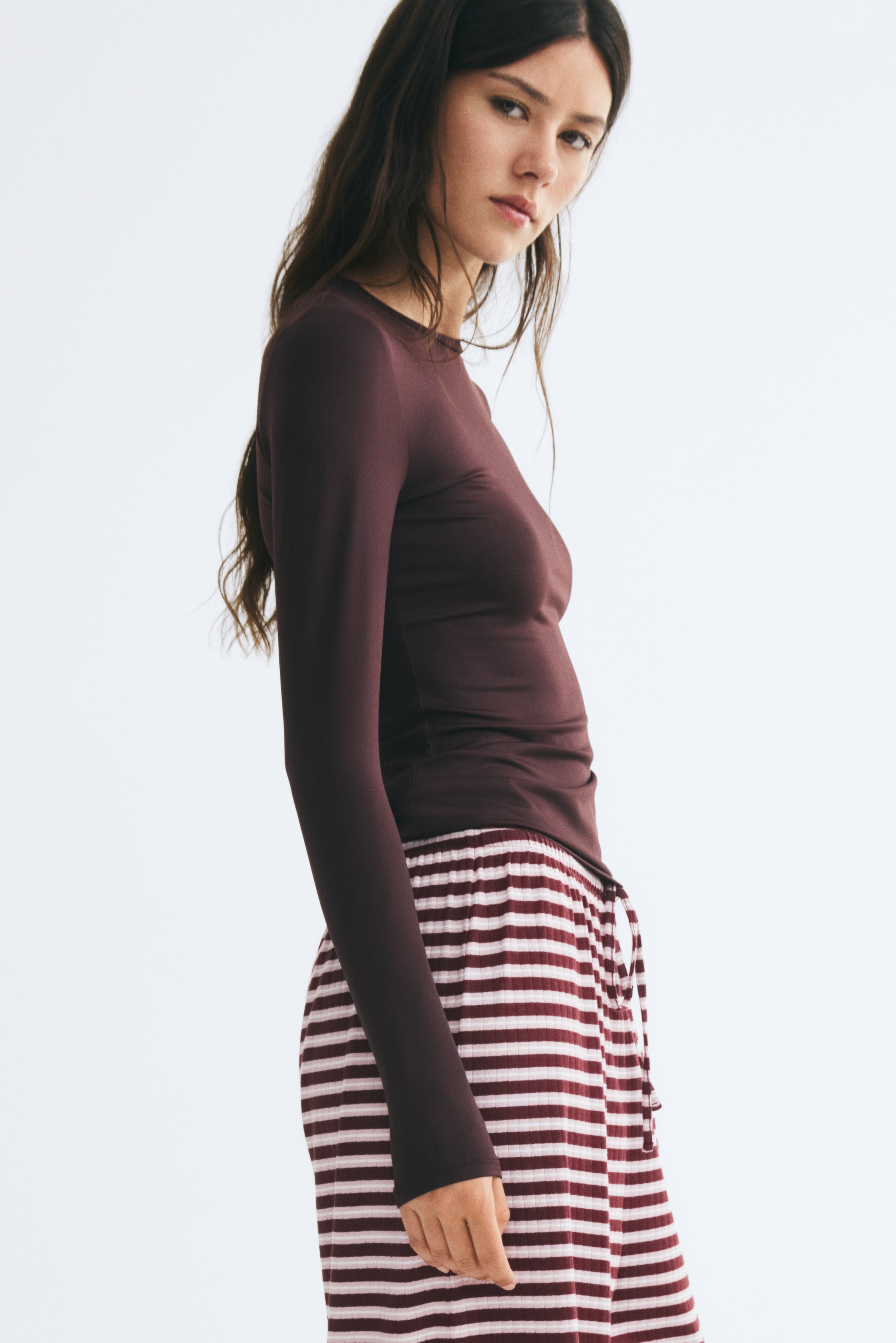 Una maglia aderente a maniche lunghe di colore bordeaux scuro in morbido jersey con un bordo stretto intorno allo scollo rotondo viene presentata dal DAVANTI.