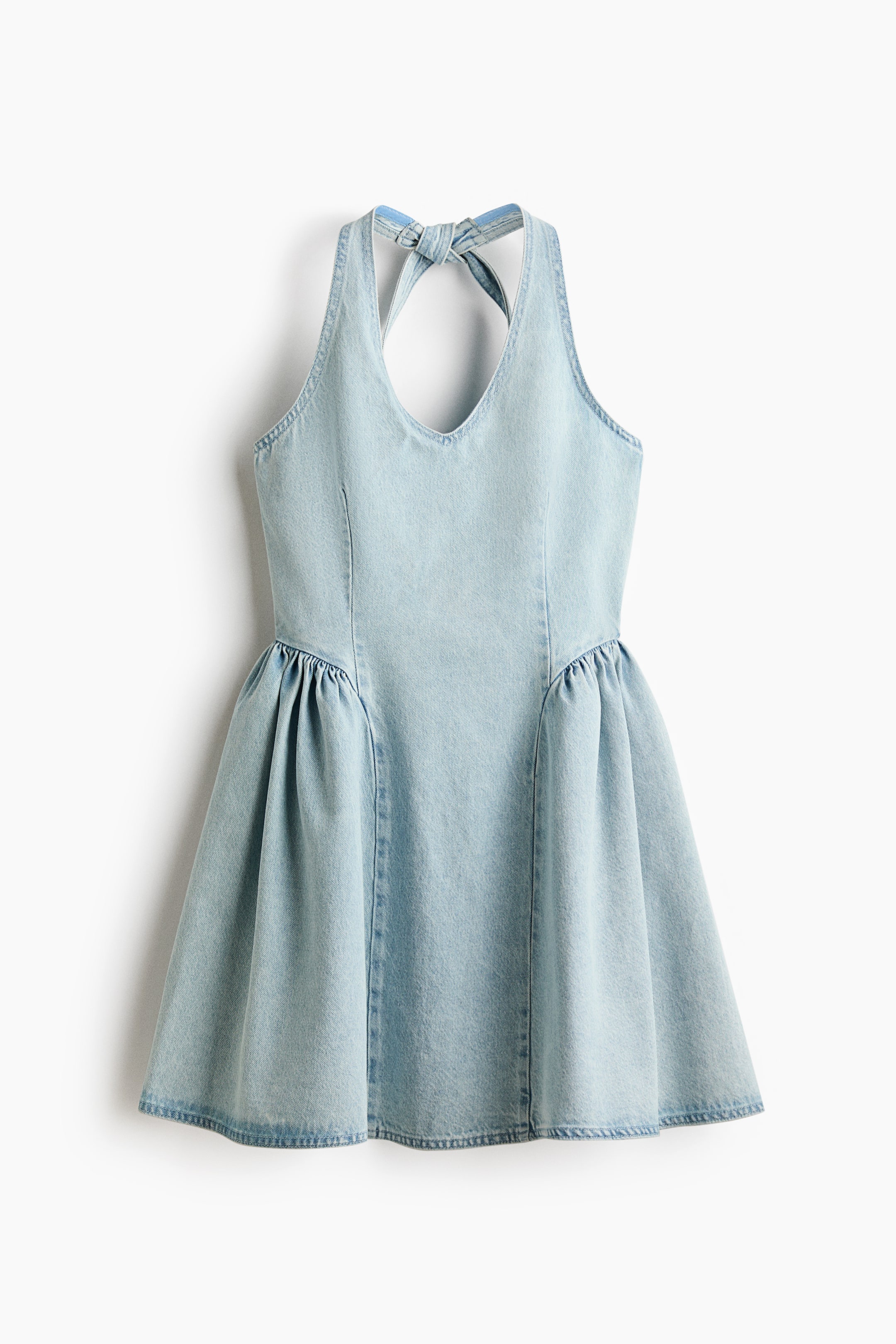 Agrandir l'image: Une robe courte en denim de coton rigide est présentée de face, avec un décolleté arrondi et de larges liens de tour de cou noués à l'arrière. Elle affiche un corsage ajusté avec des pinces à la taille pour la mise en forme et une jupe évasée avec des fronces sur les hanches pour un volume supplémentaire.