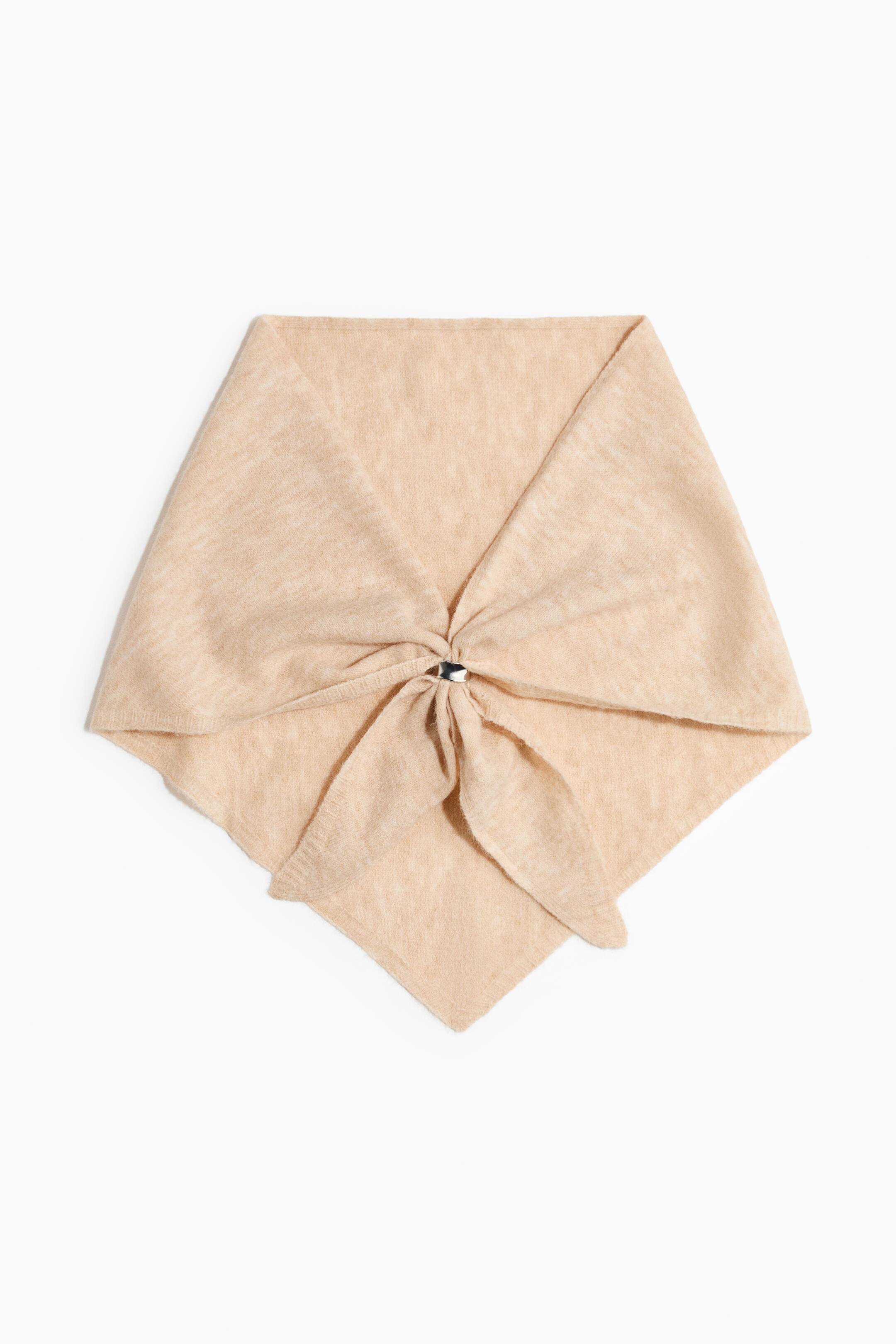 View larger image: A light beige, fine-knit triangle scarf is laid flat, facing front, with its two side ends drawn together and secured at the centre with a small, metallic silver-toned ring.