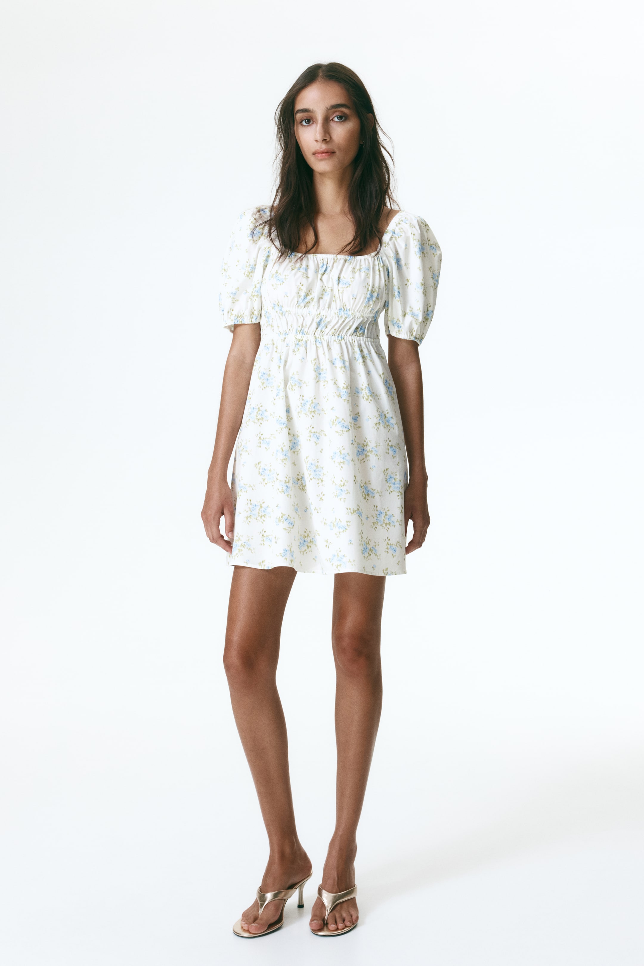 Ampliar la imagen: El vestido mini blanco presenta un patrón floral azul claro, un escote cuadrado, mangas cortas abullonadas y una cintura fruncida sobre una falda acampanada.