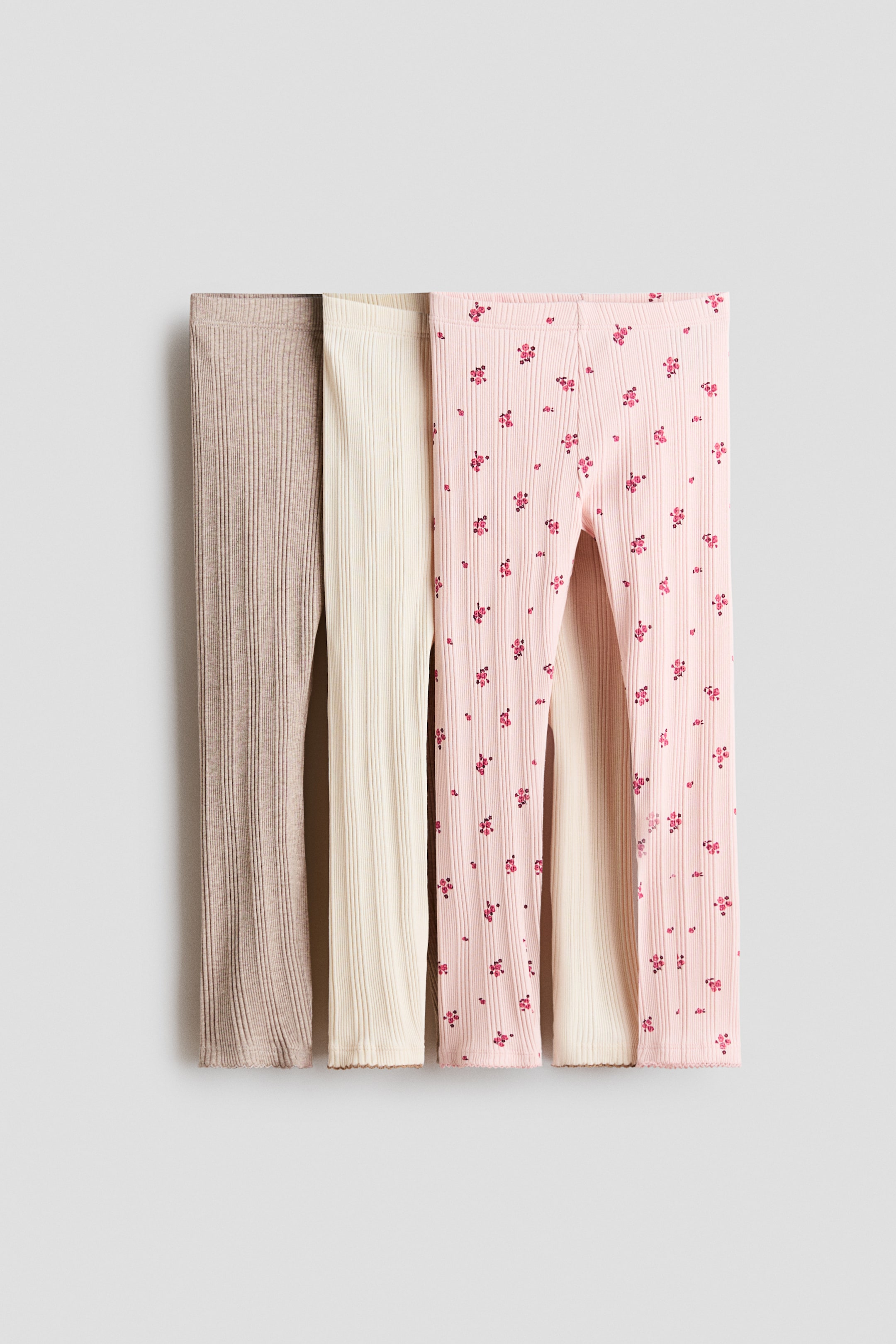 View larger image: Three pairs of ribbed leggings are laid flat, showcasing in beige, off-white, and light pink. The light pink pair features a repeated pattern of small dark pink flowers, with a scalloped hem.