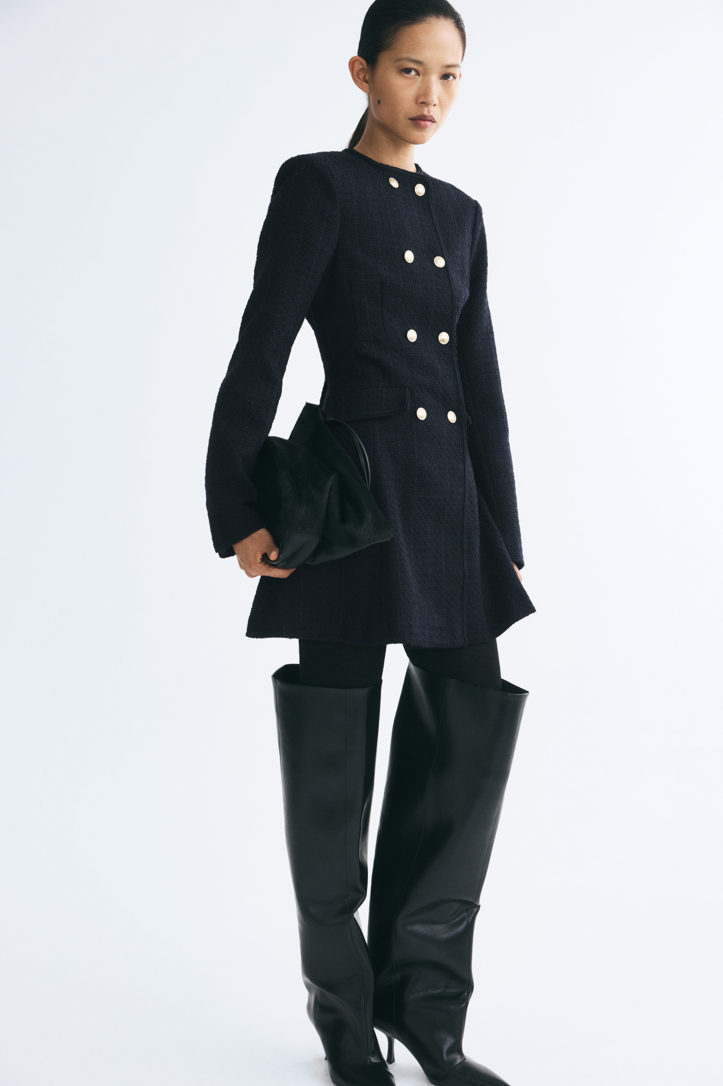 A dark navy blue tweed coat is hanging front-facing, featuring a collarless round neckline and a double-breasted closure with eight gold-toned dome buttons. The coat has a textured surface, long sleeves, and two structured waist flap pockets.