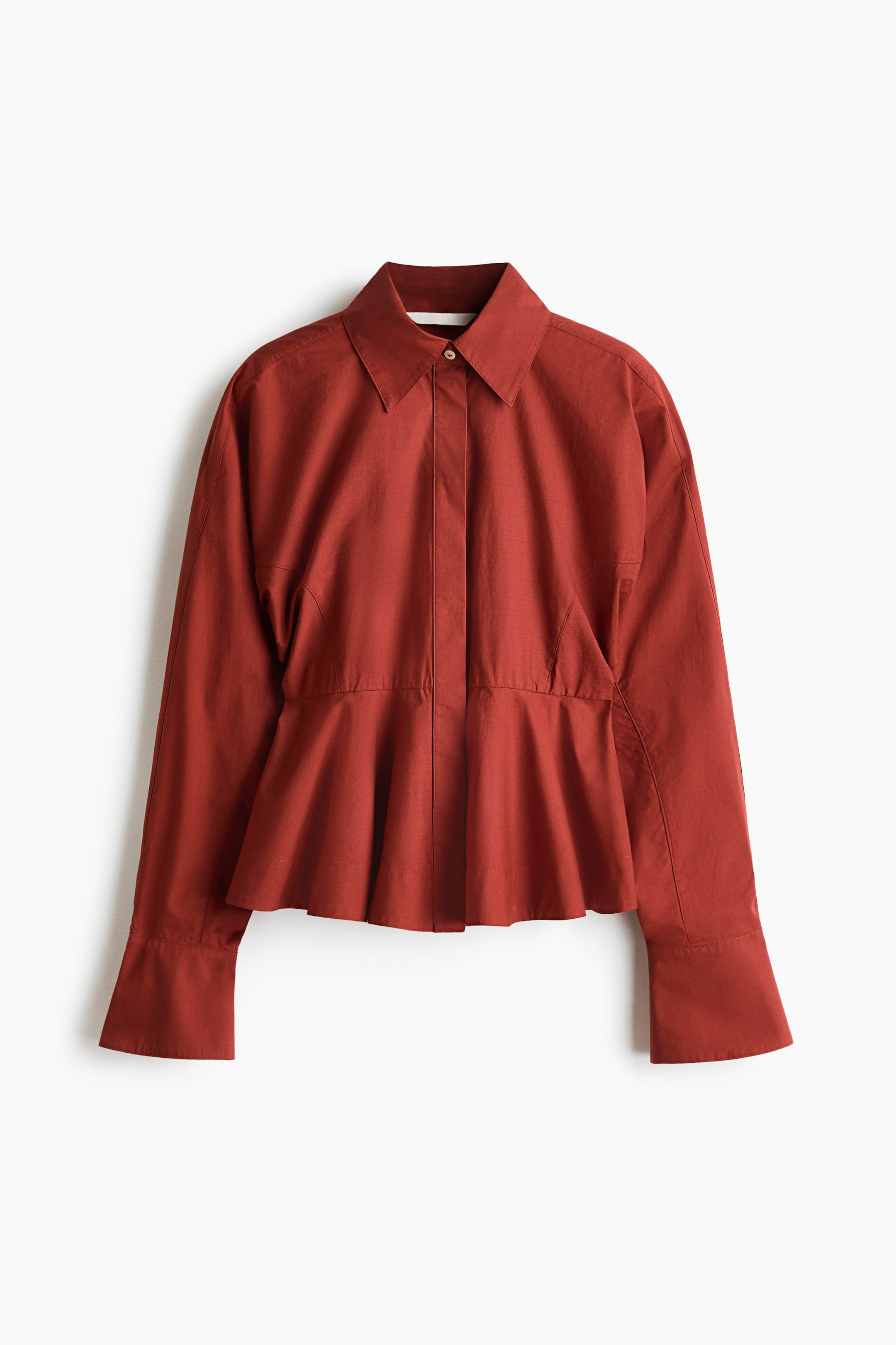 View larger image: A rust-red cotton poplin shirt is displayed facing front, featuring a pointed collar, a concealed button placket, and long batwing sleeves with wide, flared cuffs. The garment is gathered at the waist, flaring out into a structured peplum hem.