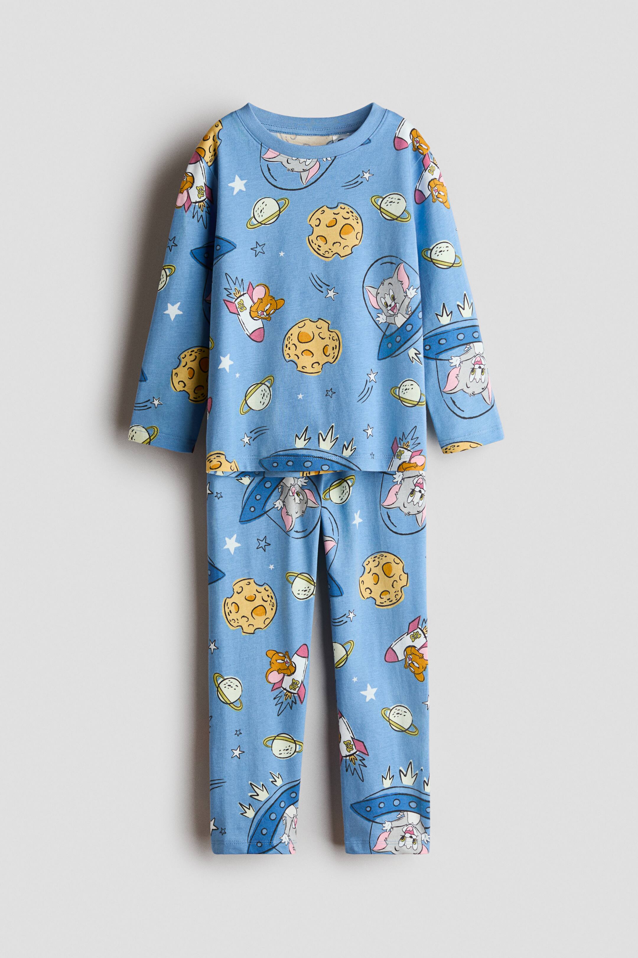 View larger image: The light blue long-sleeved pajama set is shown front-facing, featuring a space-themed print. The top and long pants depict the cartoon characters Tom and Jerry in rockets and UFOs, alongside moons, planets, and stars, with the top featuring a crew neck.