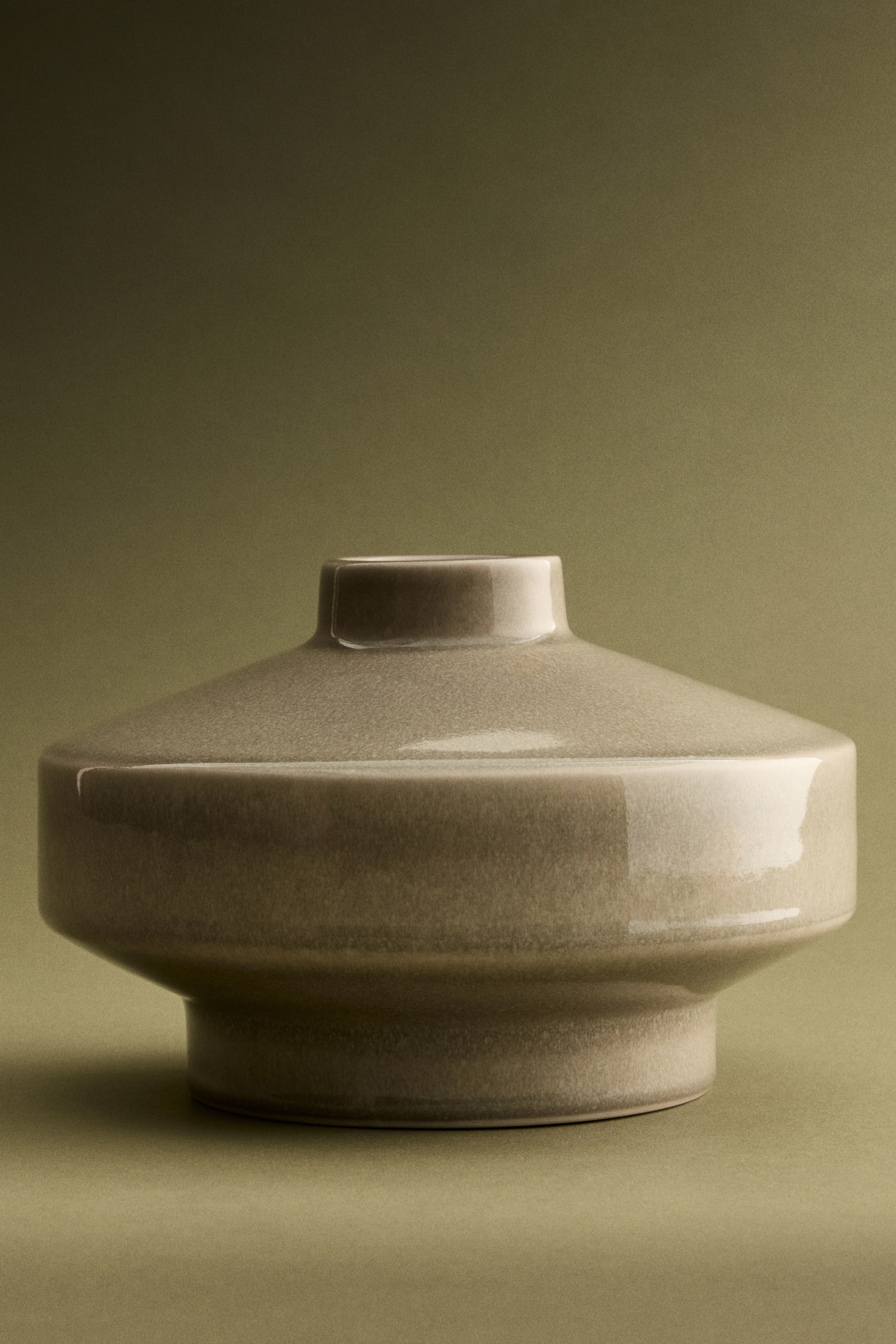 View larger image: A ceramic vase features a wide, flattened circular body with a narrow, raised neck and a slightly narrower cylindrical base, finished in a speckled, glossy taupe-grey glaze.