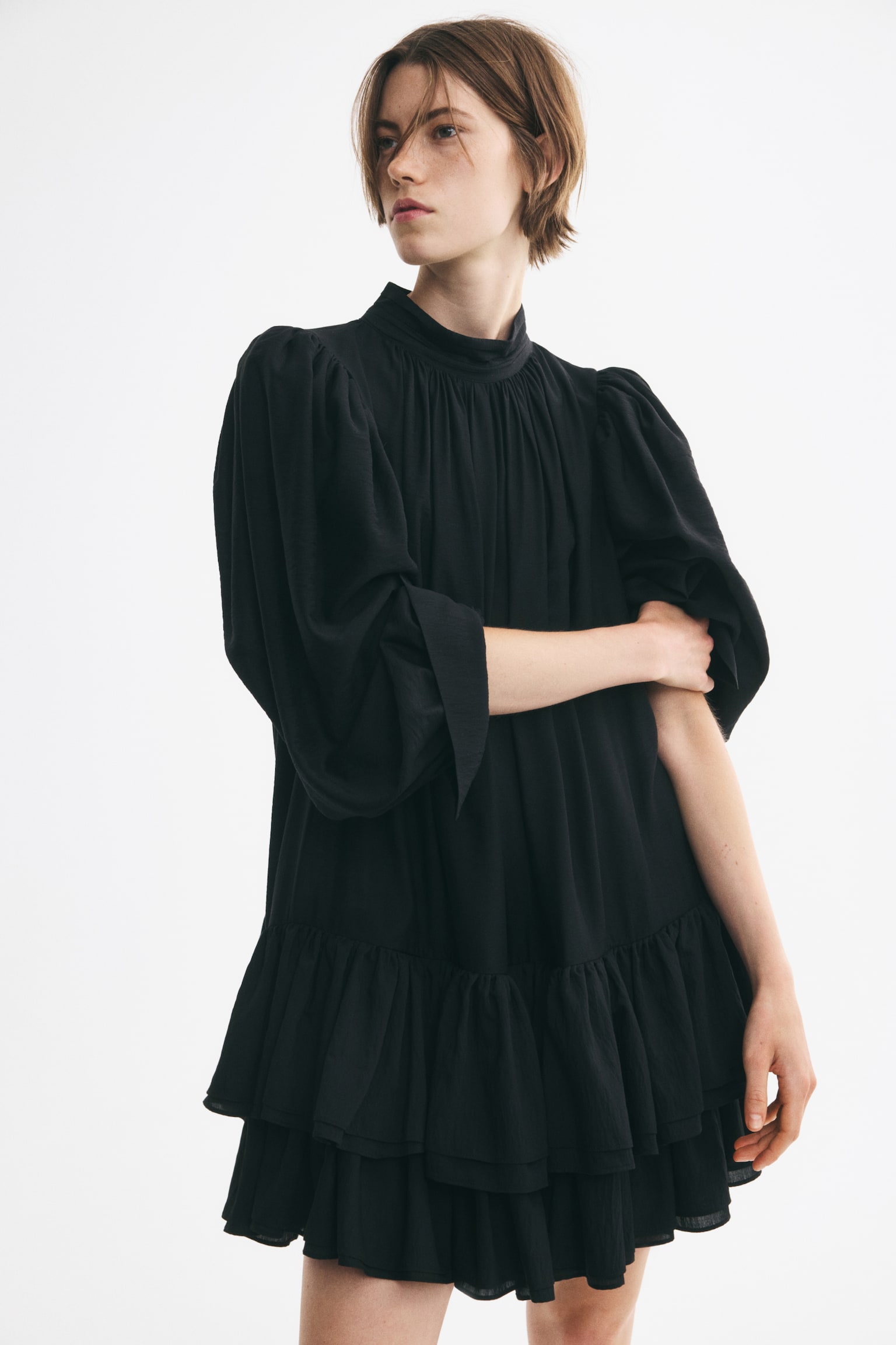 A black dress featuring a high gathered neckline, a pleated bodice, long voluminous sleeves with wide cuffs, and a two-tiered crinkled ruffle hem. - 1