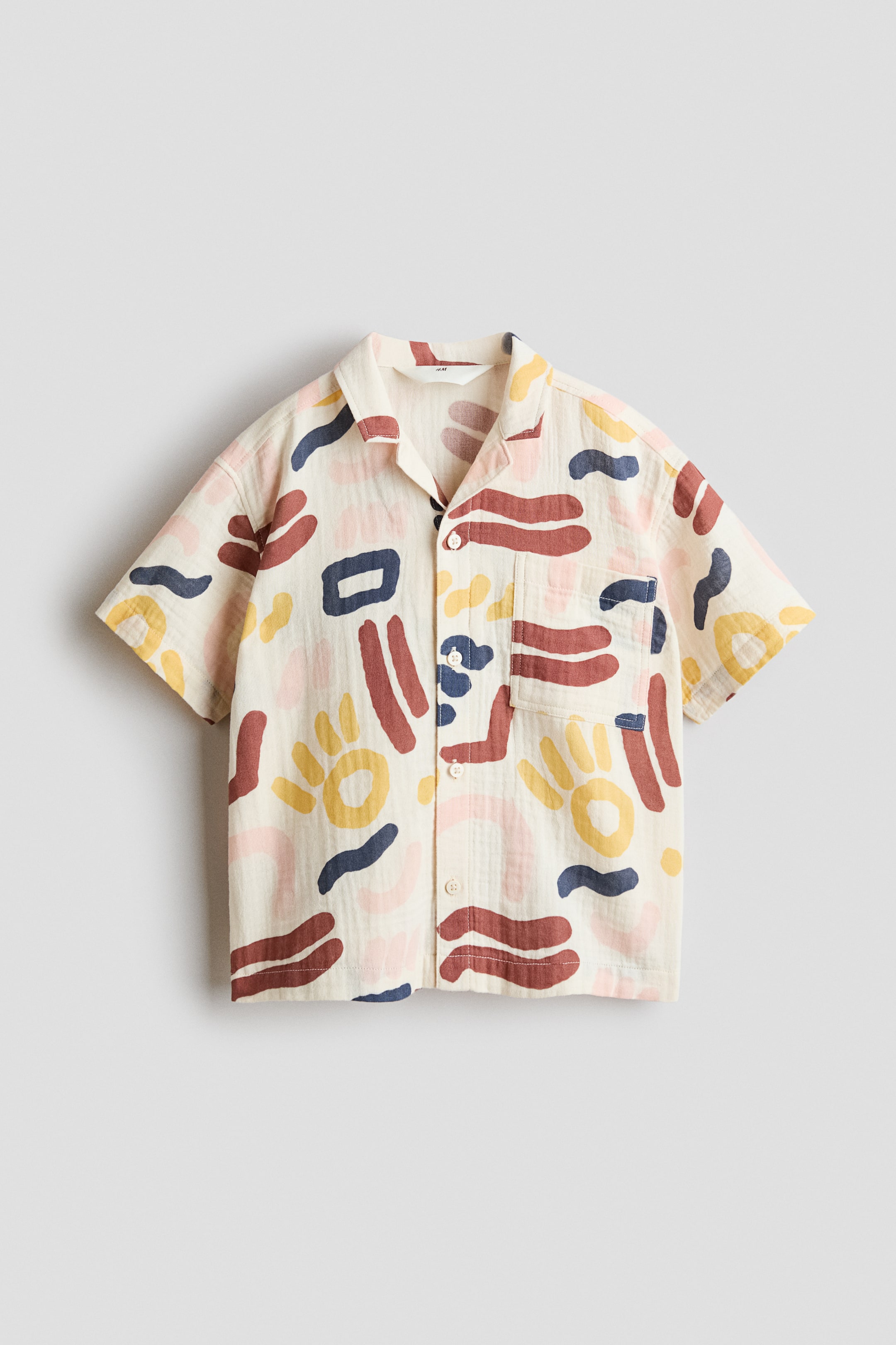 View larger image: A short-sleeved shirt is showcased FRONT facing. It features an off-white background adorned with an abstract pattern of shapes in dark red, dark blue, yellow, and light pink. The shirt is crafted with a camp collar, a button-front closure, and a single patch pocket on the left chest.
