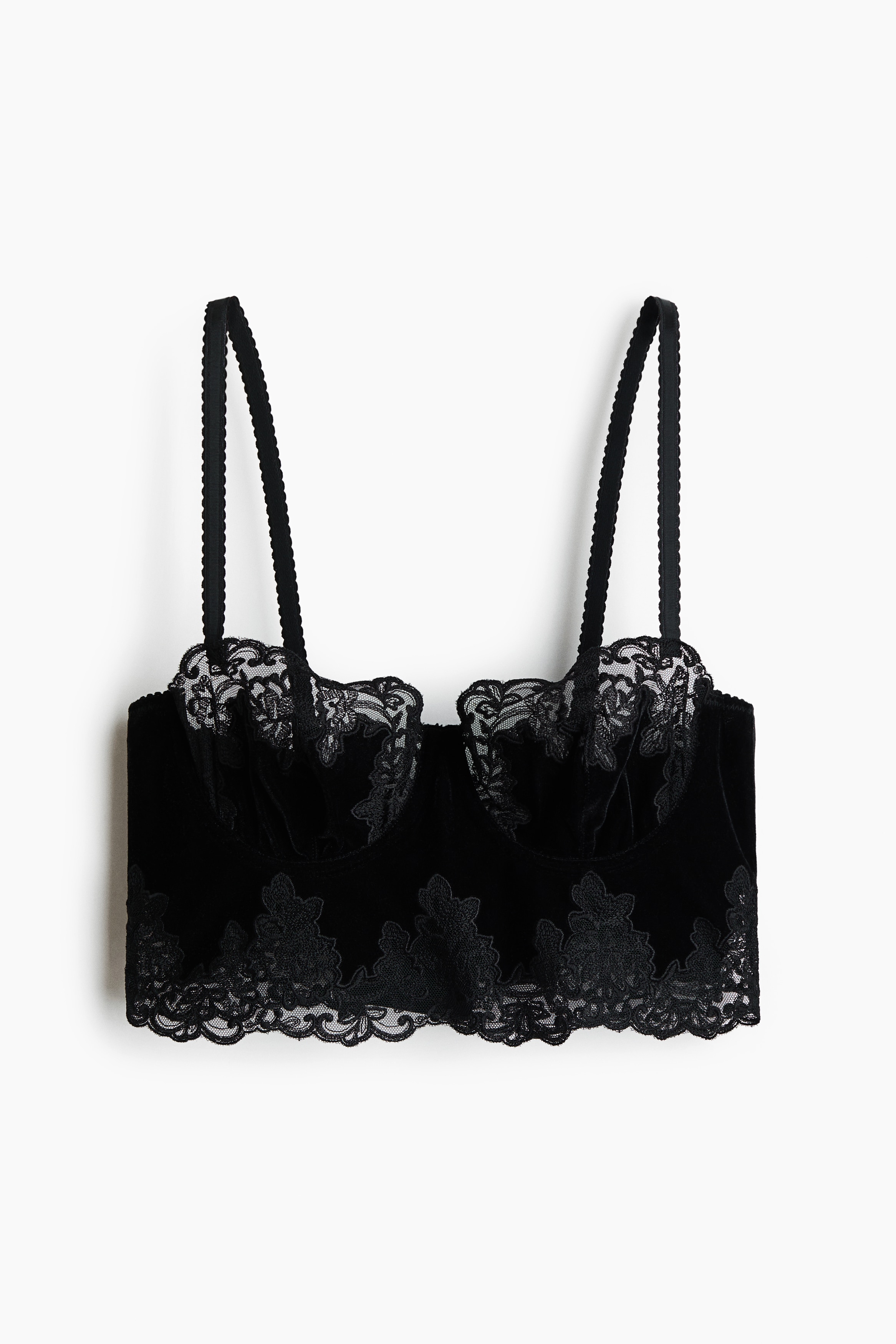 A longline bralette featuring soft velvet panels and embroidered lace detailing is being worn by the model. The design includes structured, underwired cups with a scalloped edge and thin shoulder straps.