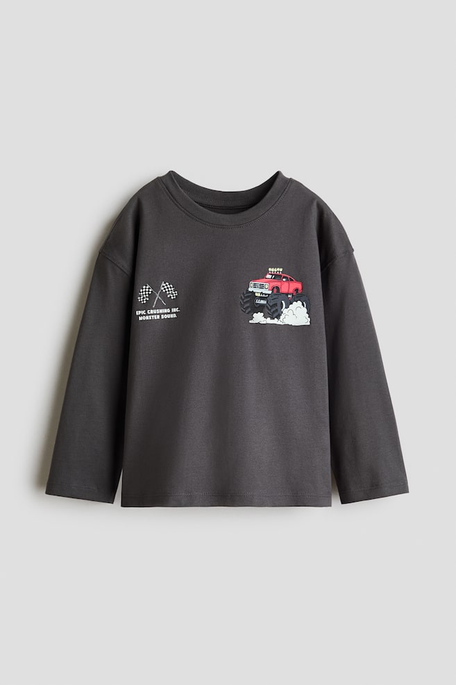 Denne mÃ¸rkegrÃ¥ langÃ¦rmede T-shirt i bomuldsjersey er vist forfra og har sÃ¦nkede skuldre samt en ribstrikket rund halsudskÃ¦ring. PÃ¥ brystet ses et trykt motiv med en rÃ¸d monstertruck pÃ¥ den ene side og krydsede ternede flag med tekst pÃ¥ den anden. - 1