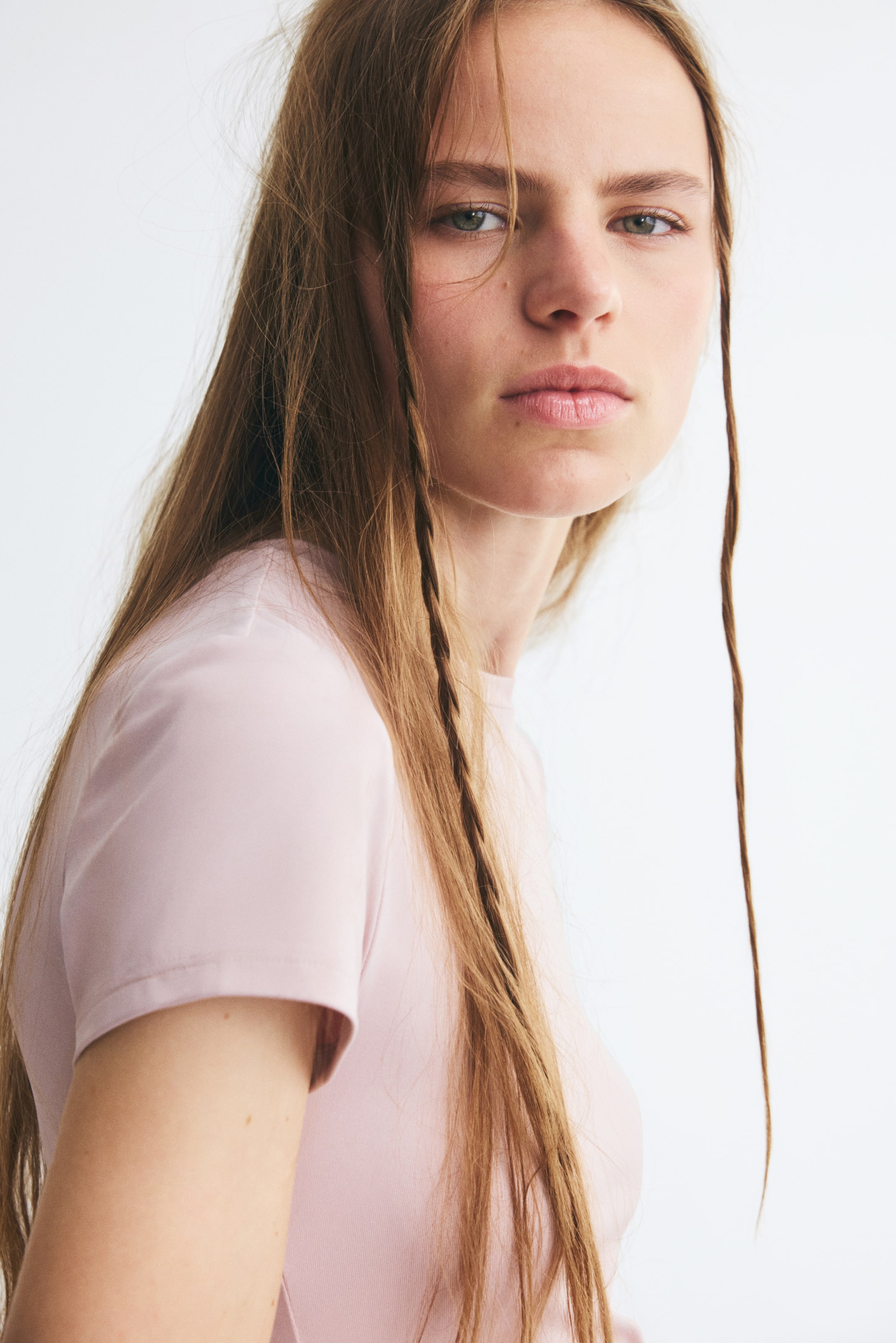 View larger image: A light pink, fitted microfibre T-shirt with short sleeves and a narrow crew neckline is being worn by the model. The close-up view highlights the smooth texture and snug fit of the garment around the shoulder and chest.