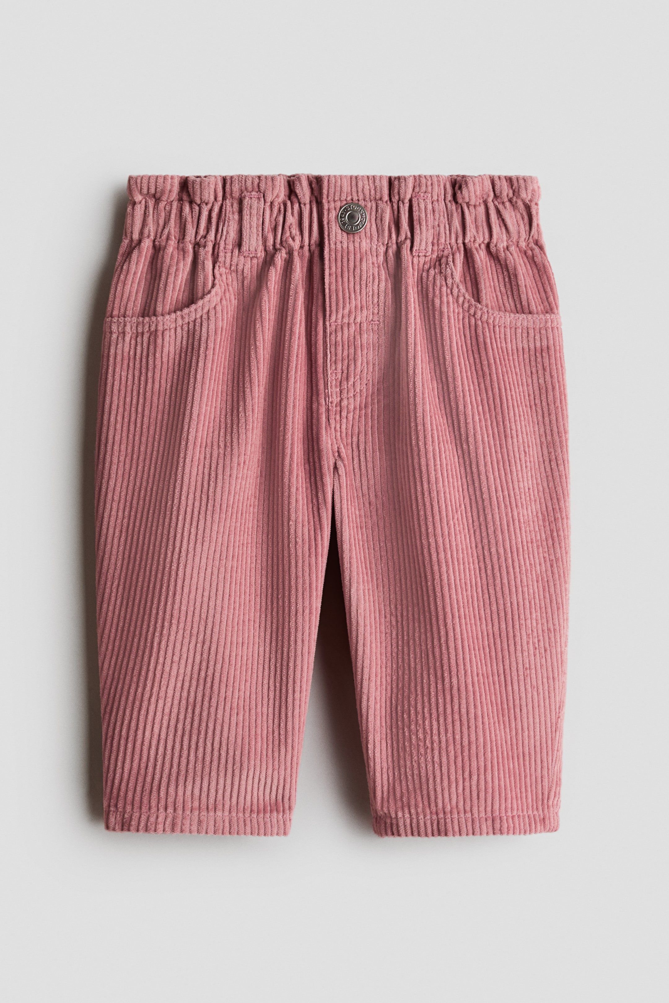 View larger image: Pink corduroy pants showcase an elasticized waistband with a single button closure at the front. They feature two angled front pockets and a prominent corduroy texture.