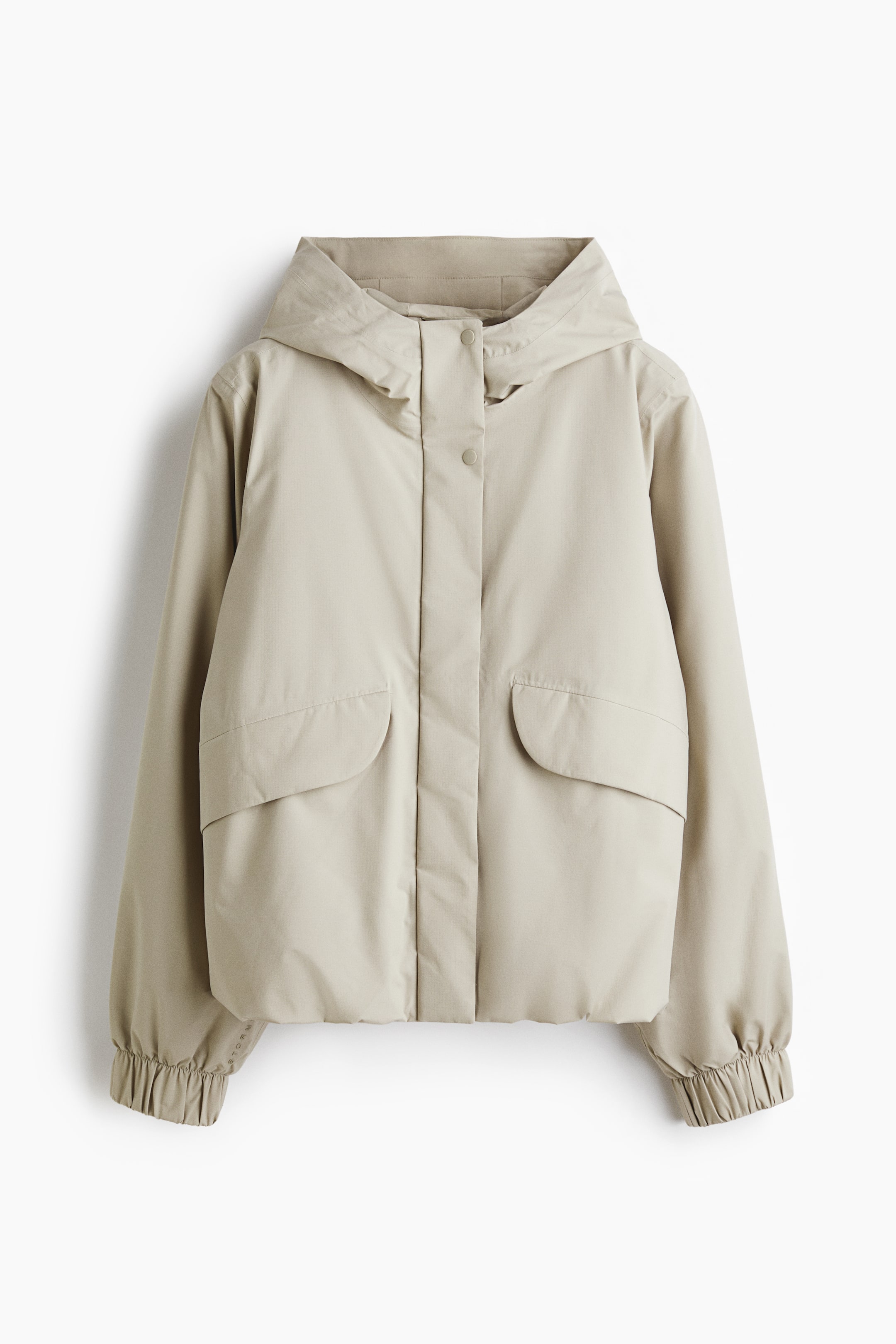 View larger image: A beige hooded jacket features a front placket with visible snap buttons, two large curved flap pockets, and elasticized cuffs on the long sleeves.