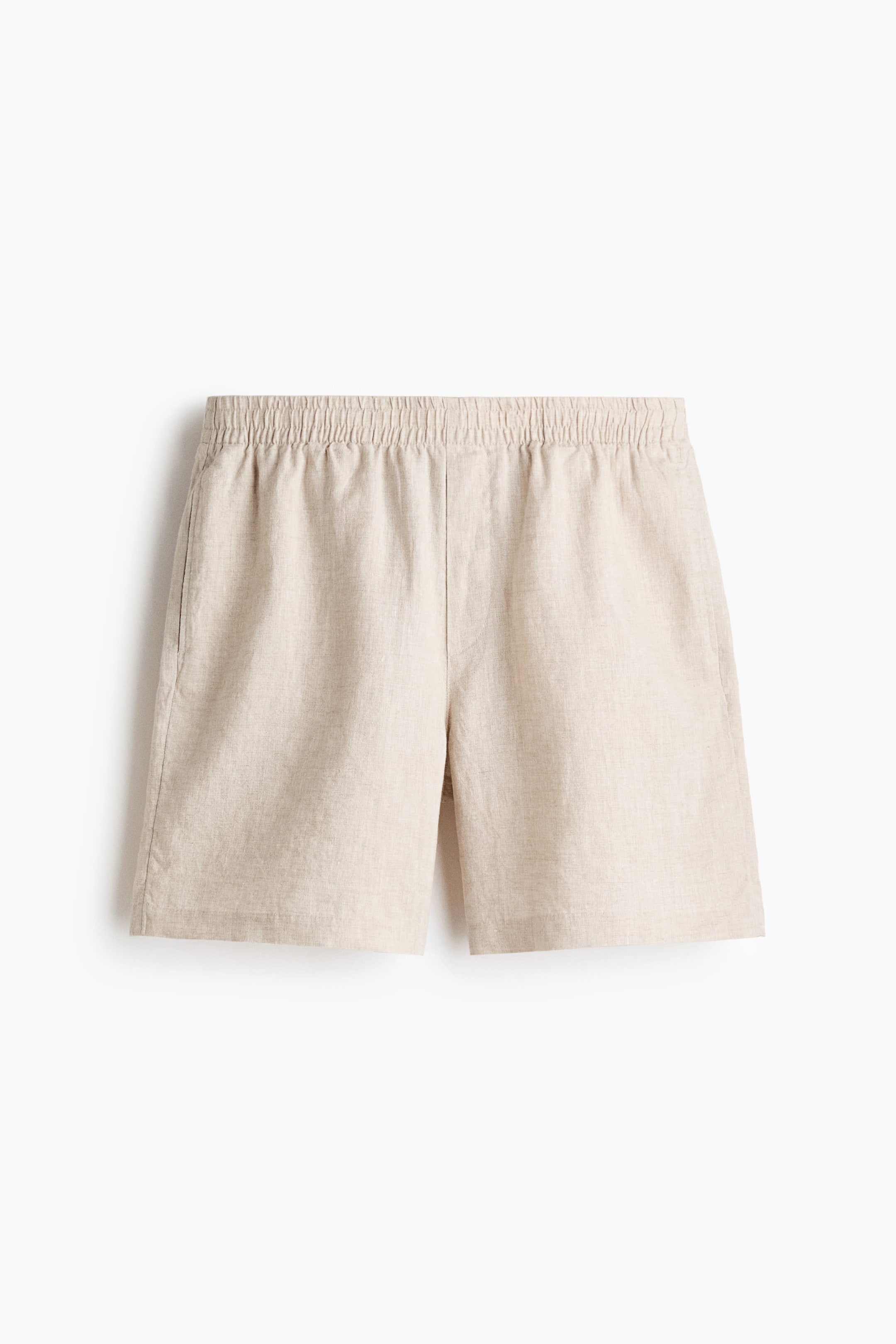 View larger image: The shorts feature a light beige, linen-look textured fabric with an elasticized, gathered waistband. Side seam pockets are visible on both sides of the front-facing shorts.