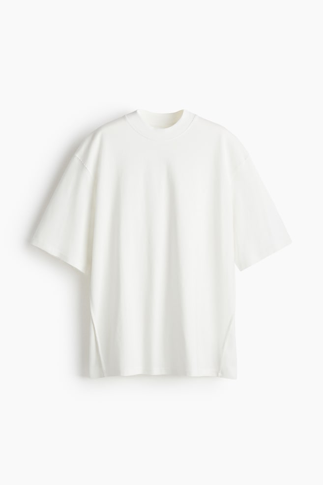 A cream oversized T-shirt in heavyweight cotton jersey is being displayed FRONT, showcasing a wide, ribbed crew neck, dropped shoulders, and elbow-length sleeves. It is also featuring a straight-cut hem and gently forward-facing, exposed side seams. - 1